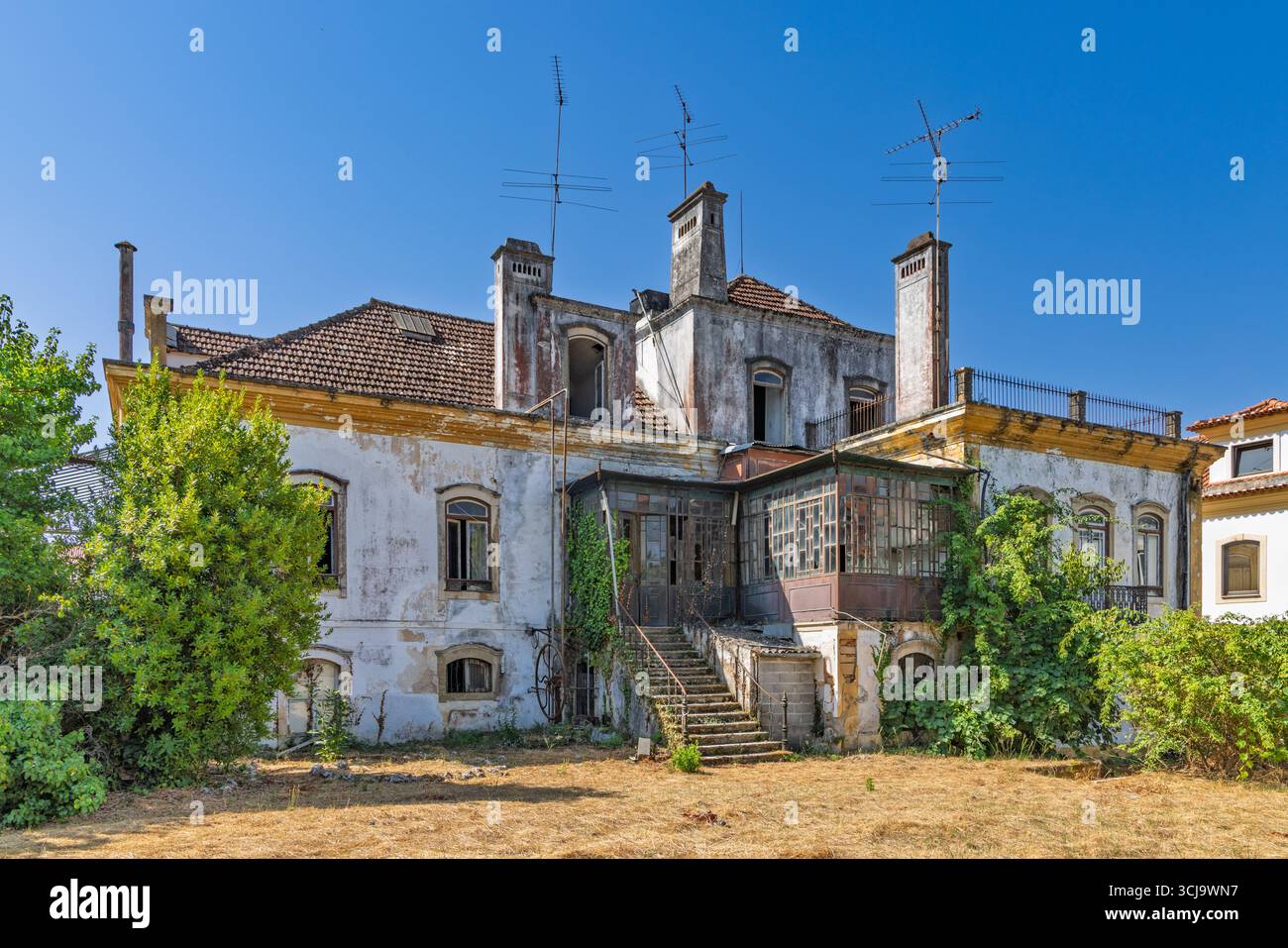 Una vecchia casa abbandonata a Tomar, in Portogallo, con una facciata intemprata e vegetazione sovrastata. Il decadimento e le caratteristiche architettoniche uniche raccontano una storia Foto Stock