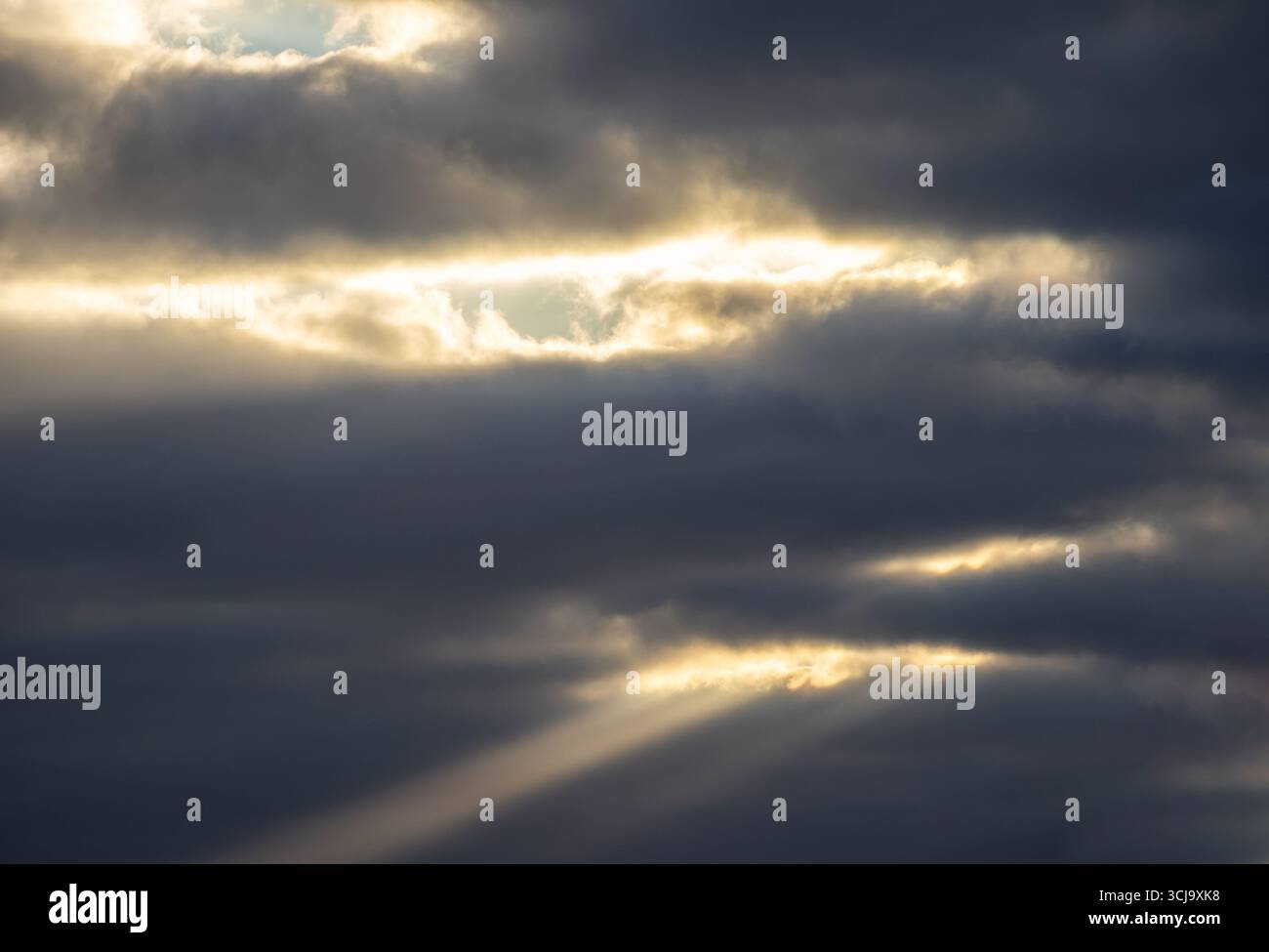 Raggi di luce del sole che si infrangono attraverso pesanti nuvole scure nel cielo Foto Stock