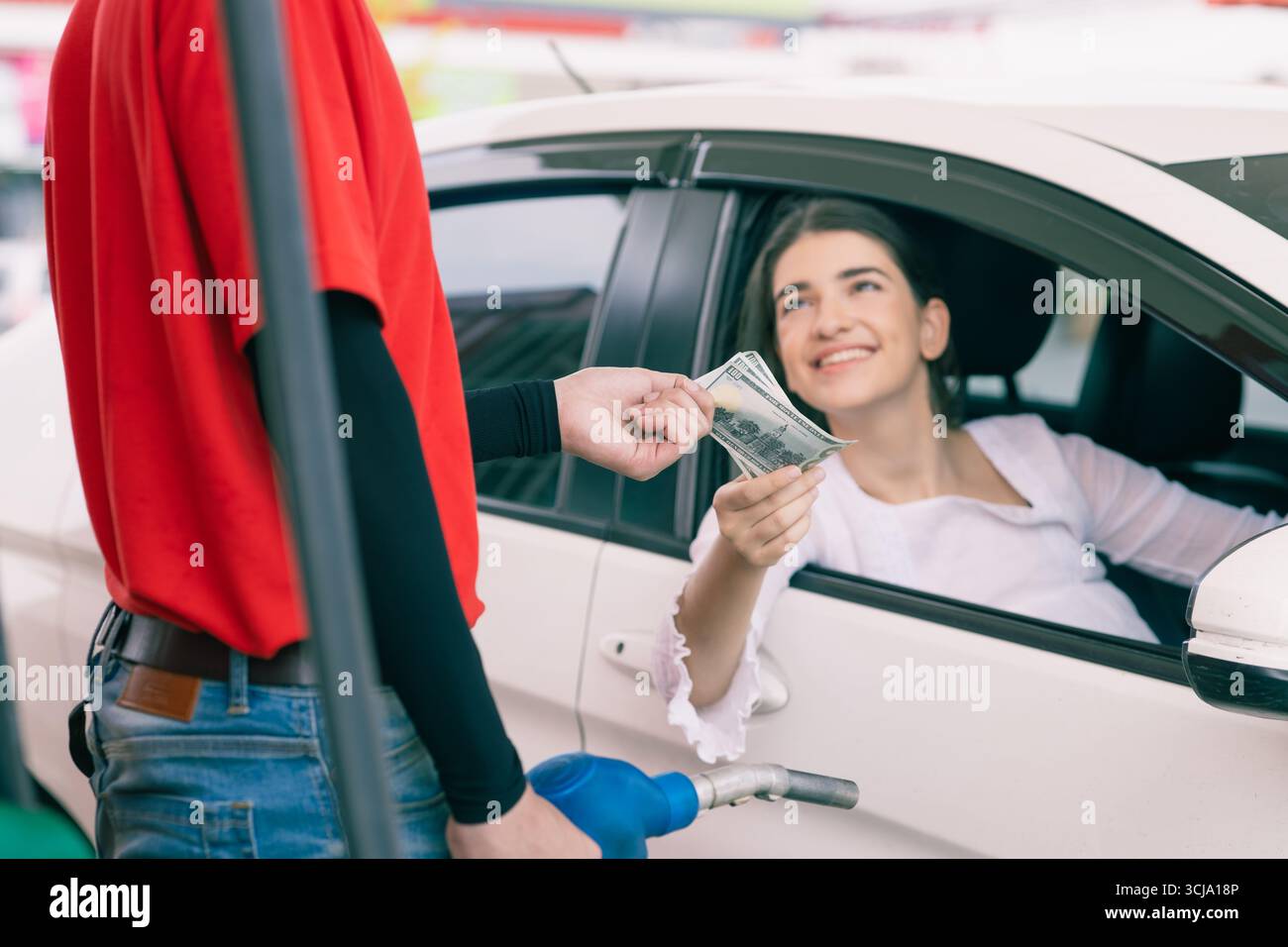 Lavoratore del personale della stazione di servizio che riceve denaro in contanti per il pagamento delle bollette del costo del carburante dal proprietario dell'auto, azienda petrolifera Foto Stock
