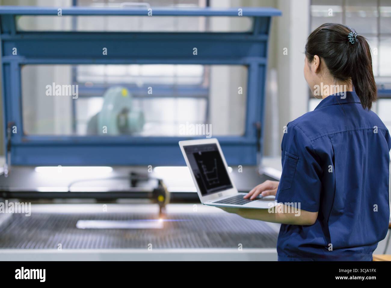 Il giovane tecnico ingegnere operante Control opera la macchina da taglio laser in metallo nella moderna fabbrica dell'industria pesante dell'acciaio Foto Stock