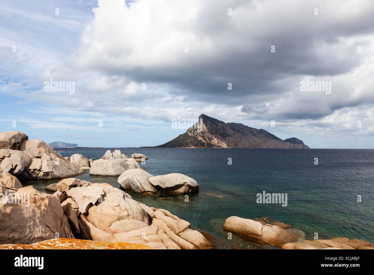 Una vista panoramica della costa rocciosa della Sardegna, Italia, con l'isola di Tavolara in lontananza. Il mare turchese e le nuvole spettacolari. Foto Stock