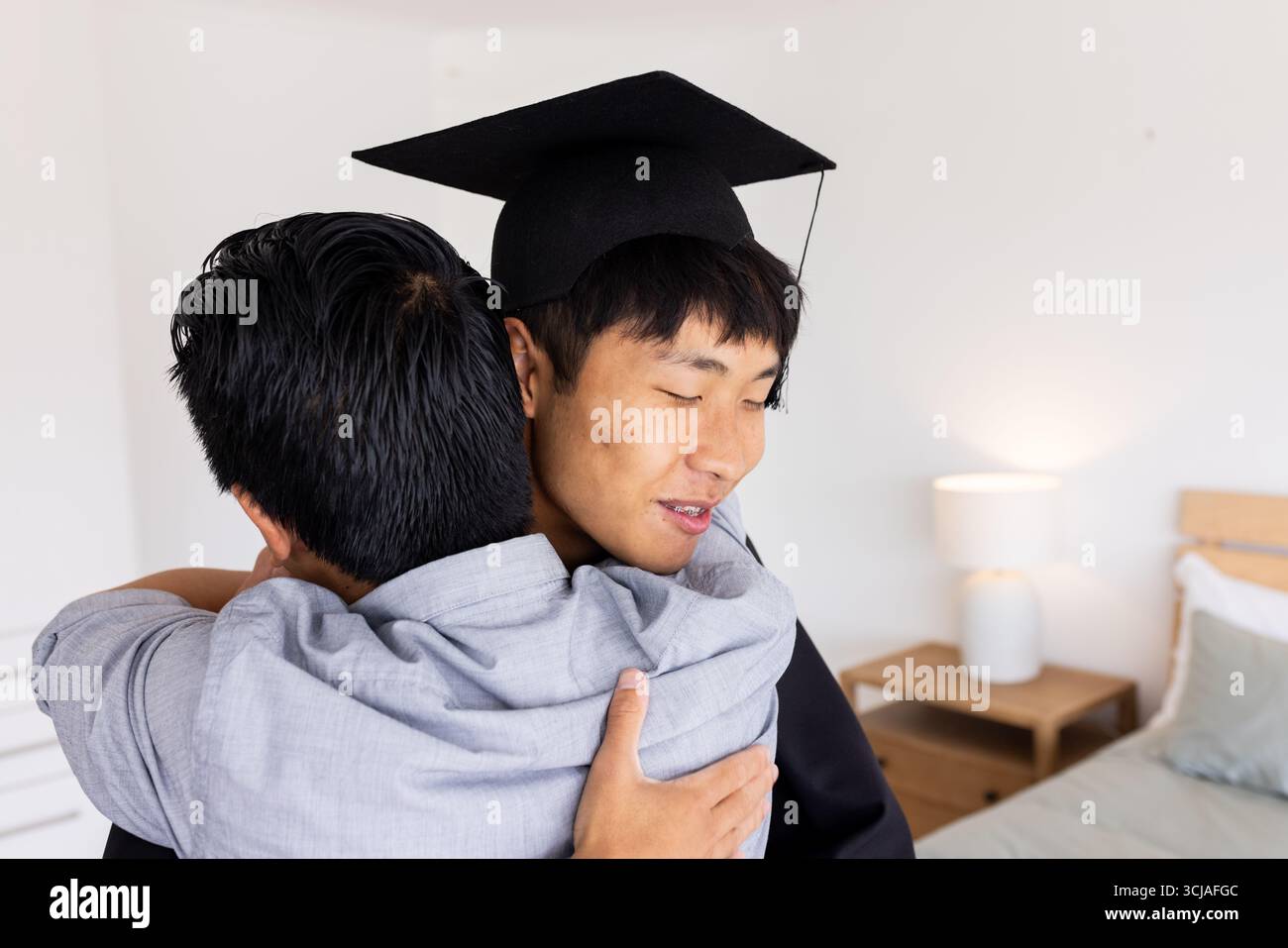 Celebrazione della laurea, giovane in cappello che abbraccia il padre a casa, si sente orgoglioso Foto Stock