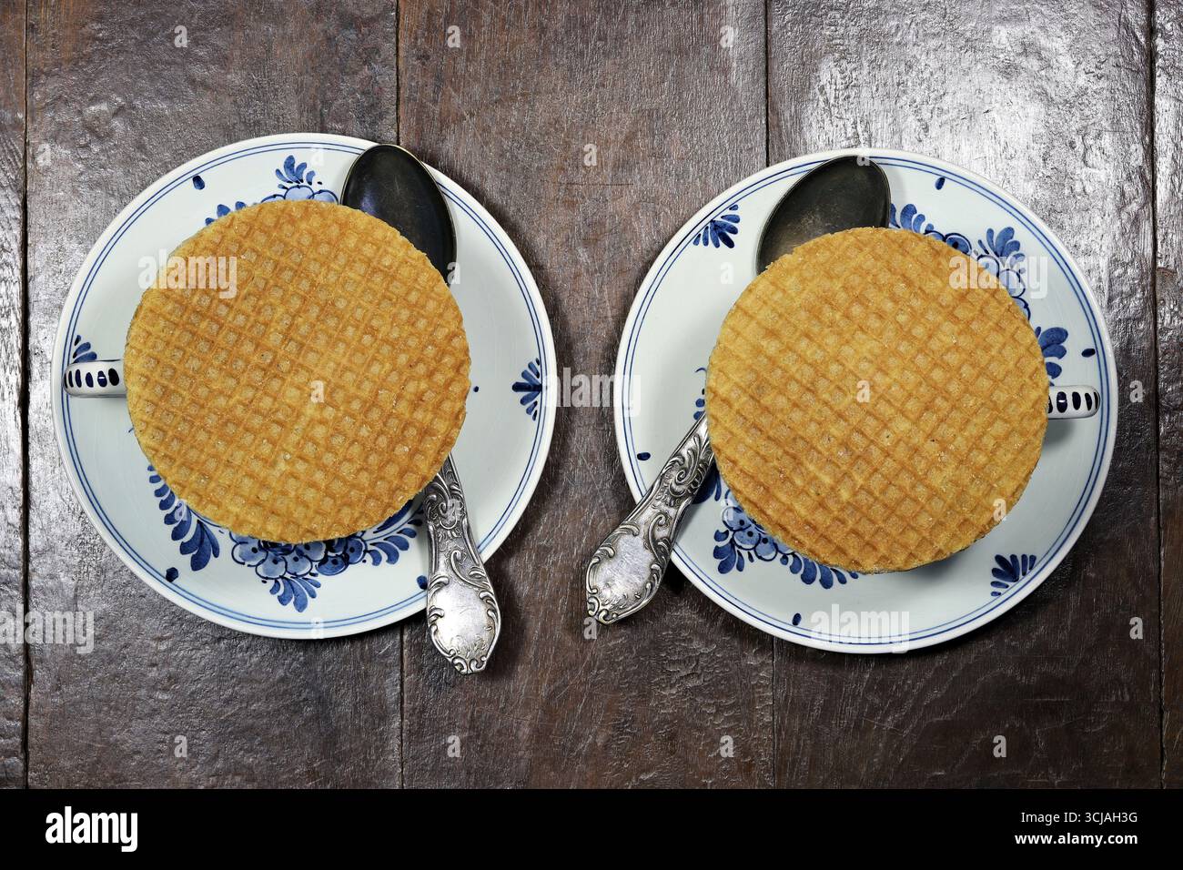 I tradizionali stroopwafel olandesi (cialde di sciroppo) sono collocati su tazze di Delftware originali su sfondo di legno Foto Stock