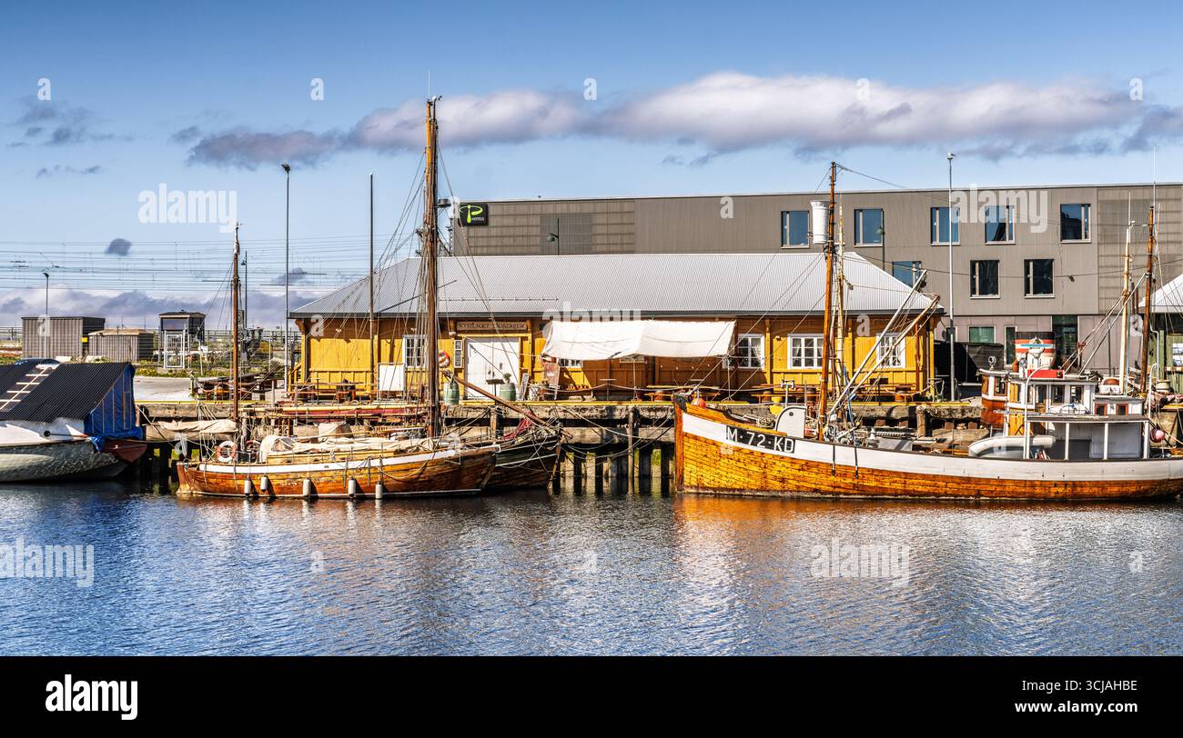Un porto panoramico con barche da pesca in legno attraccate da un molo vicino a un edificio sul mare. Foto Stock