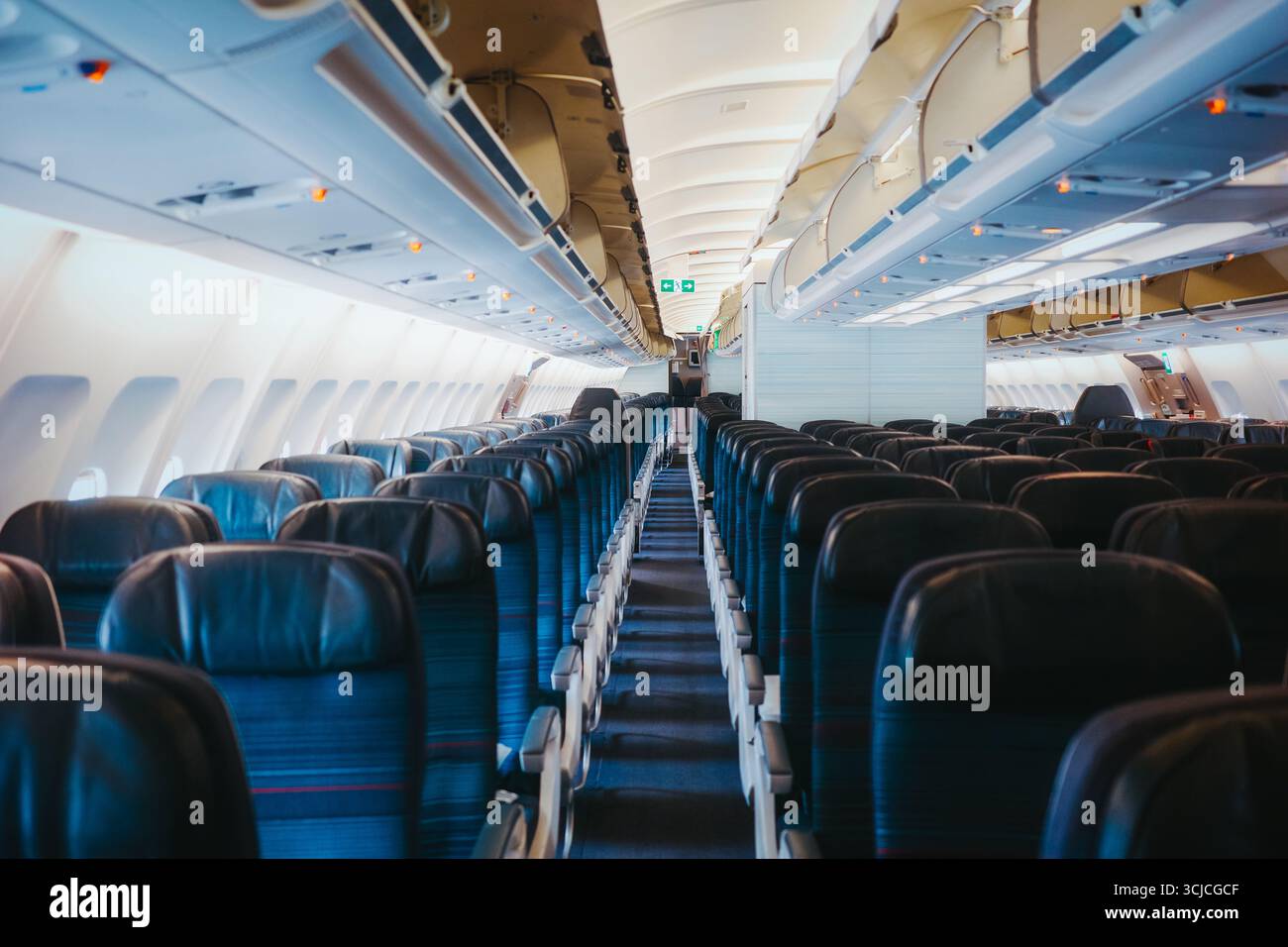 Una spaziosa cabina dell'aereo che mostra file di sedili vuoti e blu e vani a padiglione. La luce naturale scorre attraverso le finestre, offrendo un ambiente pulito e pulito Foto Stock