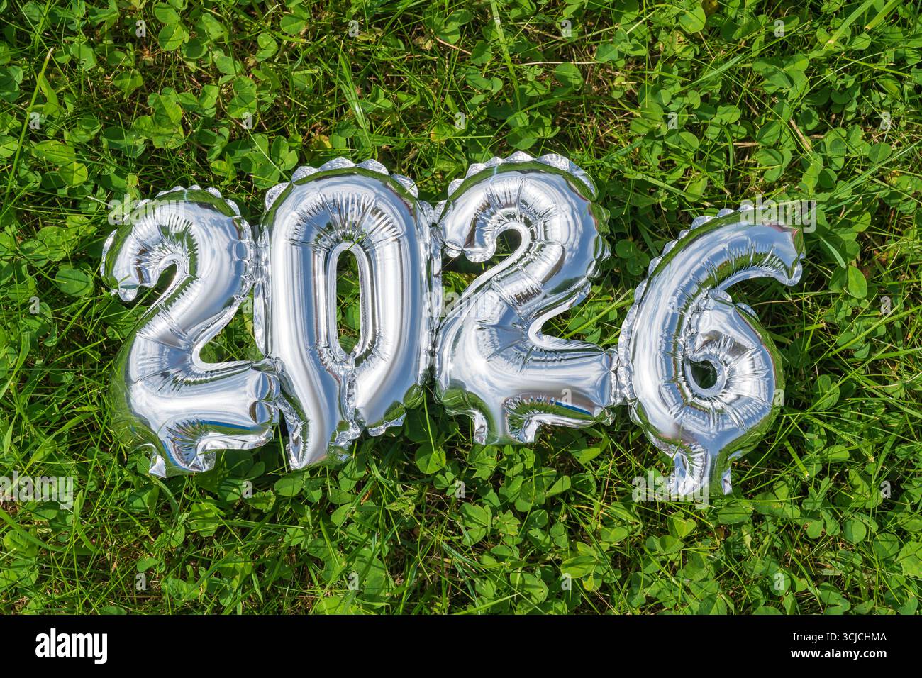 Palloncini in alluminio argentato disposti per rappresentare l'anno 2026 giacciono sulla lussureggiante erba verde, catturando un'atmosfera festosa e celebrativa, perfetta per Capodanno o per il giorno Foto Stock