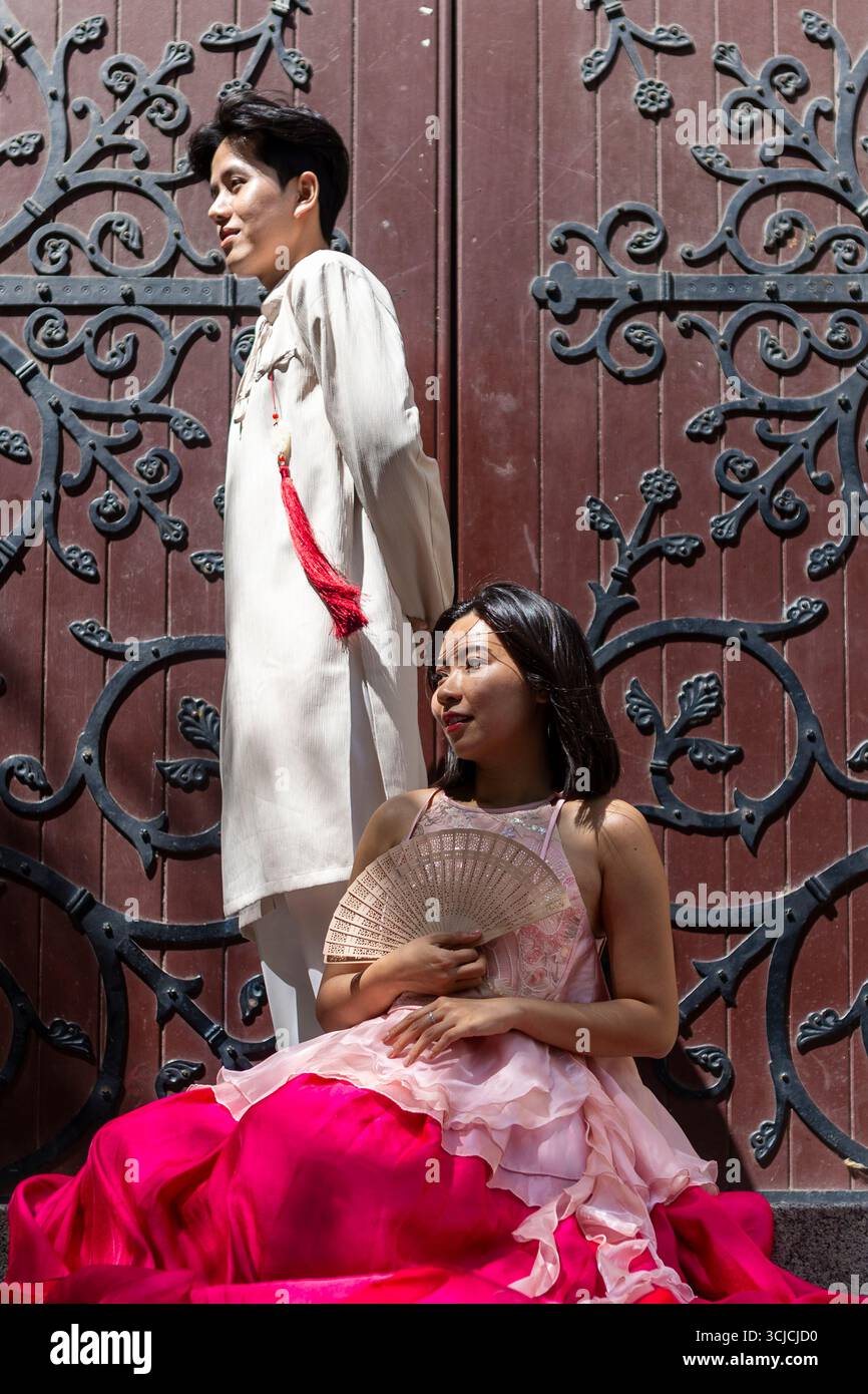 Una coppia vietnamita pone elegantemente un abbigliamento tradizionale contro una intricata porta storica di Melbourne. La scena fonde il patrimonio culturale con il nostro Foto Stock