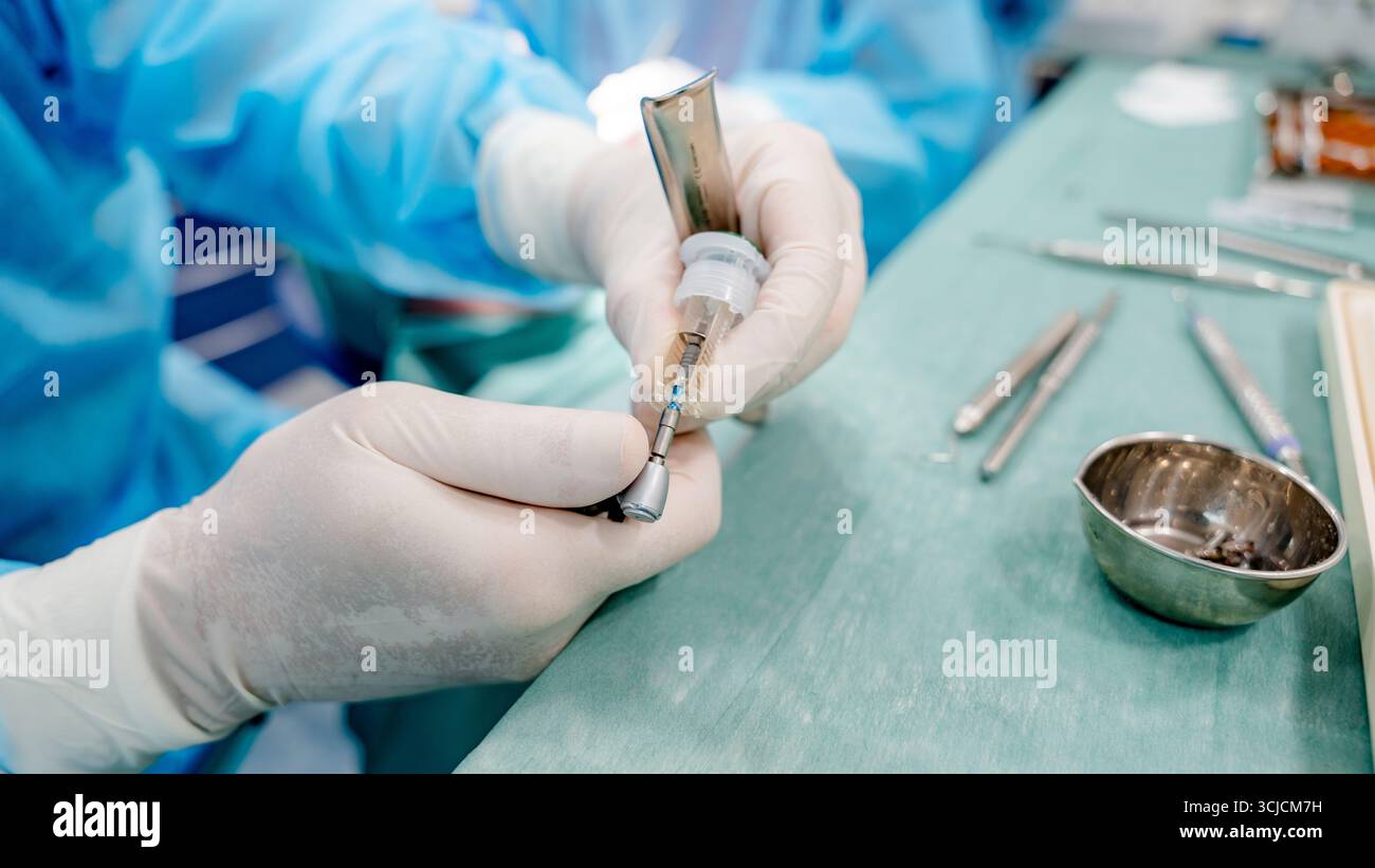 Immagine che raffigura una procedura di impianto dentale in un ambiente clinico. Un dentista in scrub blu sta utilizzando strumenti precisi per garantire un posizionamento ottimale Foto Stock