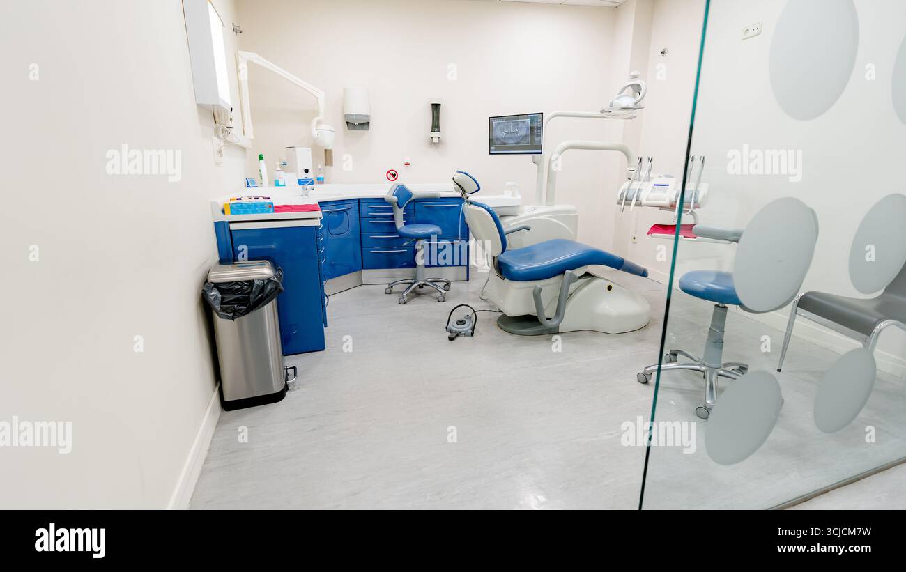 Moderno studio dentistico con uno schema colore blu e bianco, completo di sedia dentale avanzata, strumenti e attrezzature, che enfatizzano la pulizia Foto Stock