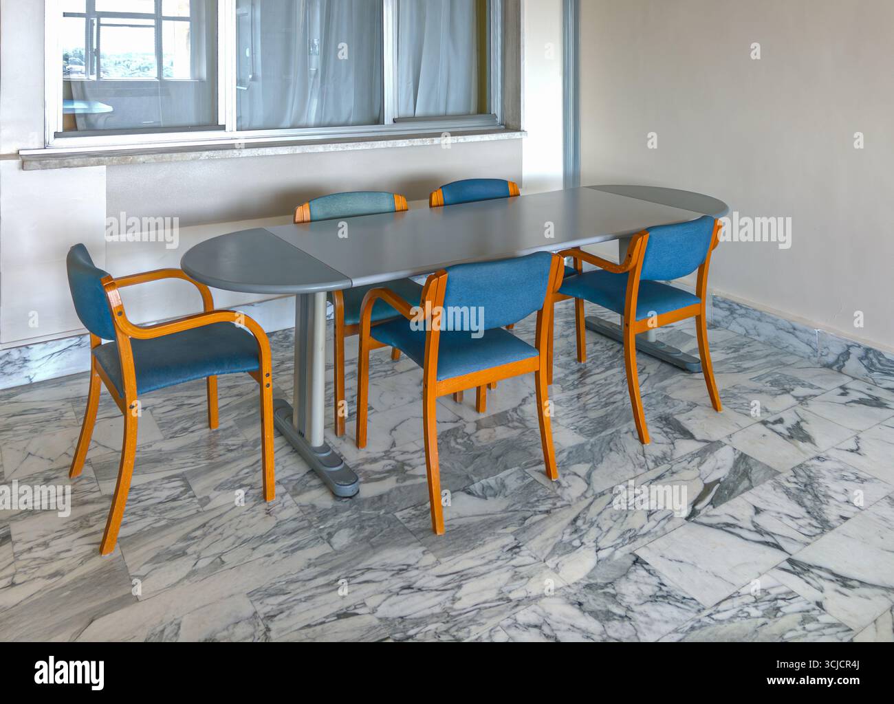 Tavolo ovale con sedie in legno rivestite in tessuto blu su pavimento in marmo bianco venato nero nella sala riunioni dell'ufficio Foto Stock