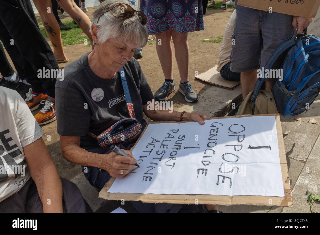 Londra, Regno Unito. 6 settembre 2025. Una donna siede sul terreno durante una protesta pubblica, scrivendo un segno che dice "io SONO CONTRARIO AL GENOCIDIO e SOSTENGO L'ATTIVISMO PALESTINESE. La scena include altri dimostranti, zaini e materiali di protesta. L'immagine cattura l'espressione personale e l'azione collettiva a sostegno dei diritti palestinesi. Difendere la protesta delle nostre giurie per la proscrizione dell’azione contro la Palestina, con oltre 1000 persone che si impegnano a tenere dei segnali contro il divieto dei laburisti e a dimostrare sostegno al gruppo proscritto. Penelope Barritt/Alamy Live News Foto Stock