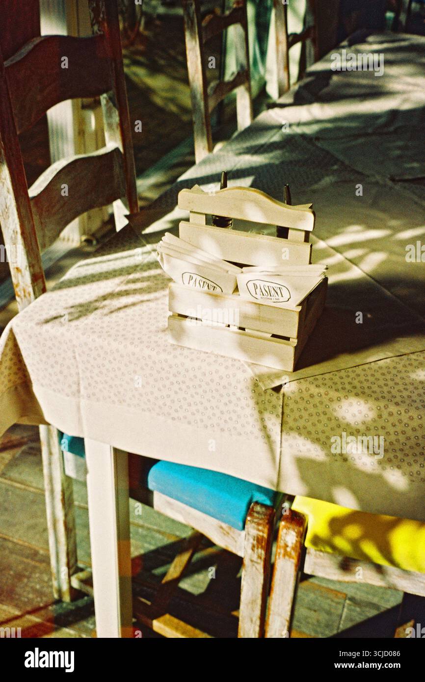 Fotografia analogica calda di un tavolo da ristorante vuoto con luce solare e ombre, che crea una natura morta minimalista nostalgica con toni morbidi e texture ricca Foto Stock