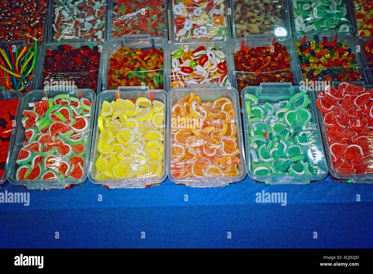 Fotografia analogica notturna di una bancarella di caramelle in un mercato all'aperto, con dolci colorati in gelatina esposti in contenitori aperti. Foto Stock