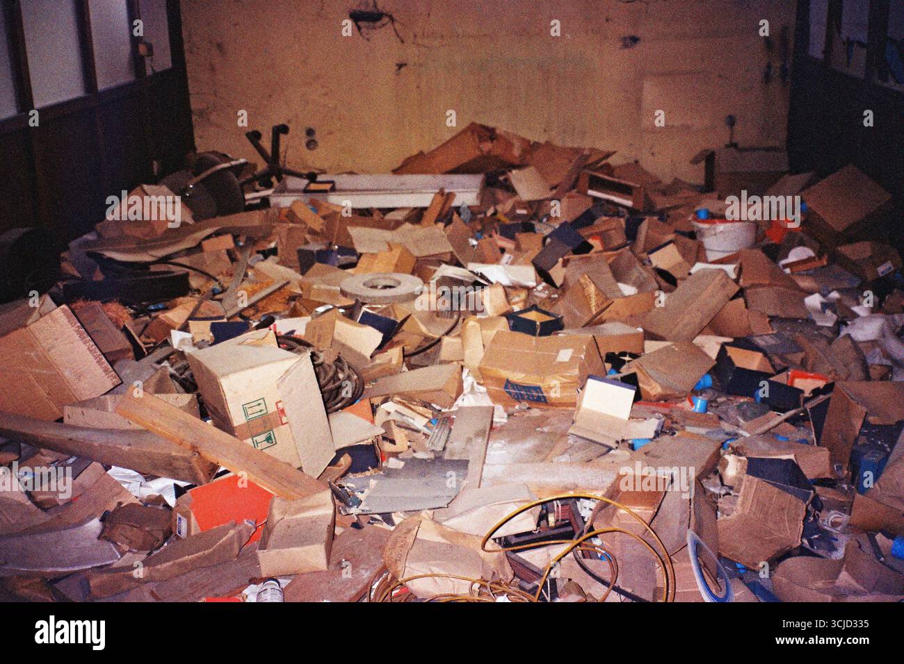 Oggetti scartati sparsi all'interno di una fabbrica abbandonata, che rivelano strati di decadimento industriale, negligenza e oggetti di uso quotidiano dimenticati in un flash analogico Foto Stock