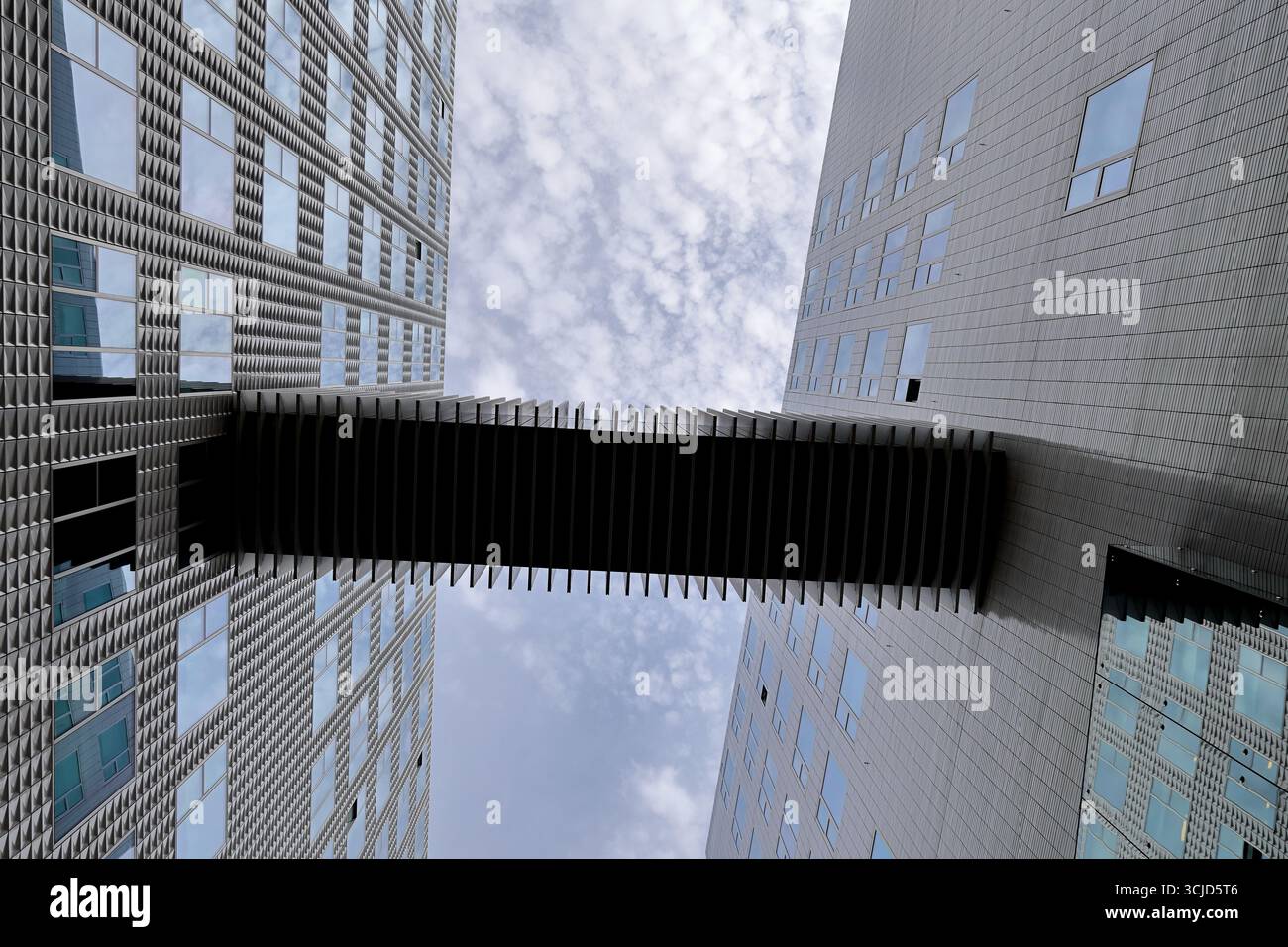 Ponte sospeso pedonale con alette a distanza ravvicinata che si estendono su due torri di uffici a IJDock, Amsterdam, Paesi Bassi, visto verso l'alto contro nuvole testurizzate. Foto Stock