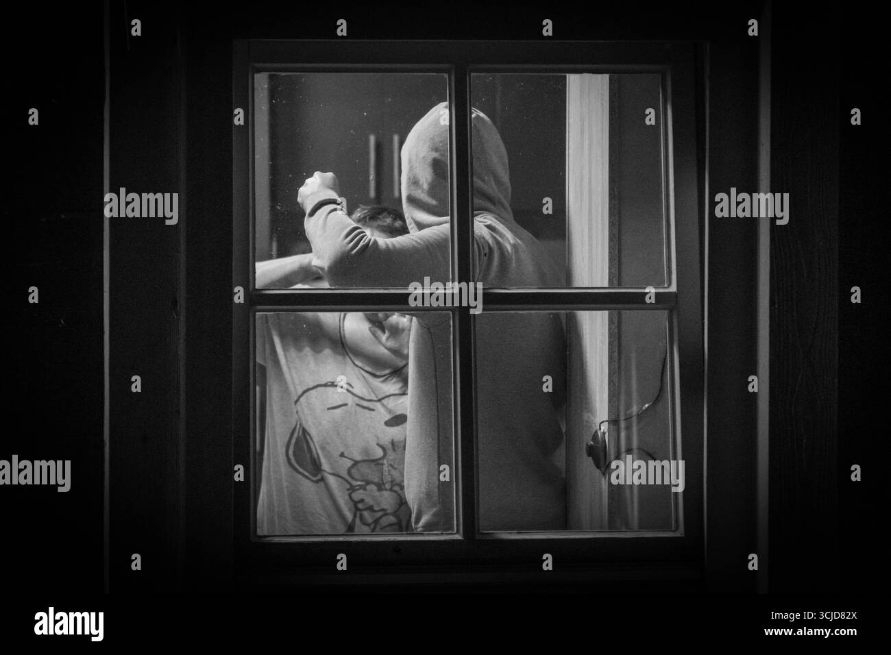 Baviera, Germania - 6 settembre 2025: Un uomo in felpa con cappuccio attacca una persona nella sua casa. L'immagine simbolica illustra violenza, aggressione e minacce all'interno delle proprie quattro mura *** Ein Mann im Hoodie attackiert eine person im eigenen Haus. DAS Symbolbild verdeutlicht Gewalt, Überfall und Bedrohung in den eigenen vier Wänden Foto Stock