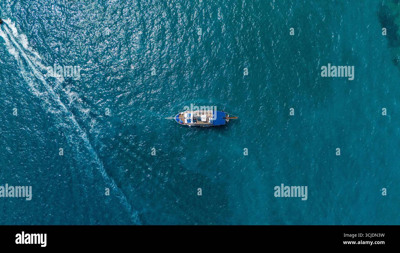 Zante, Grecia, vista aerea di una singola barca che galleggia nel turchese Mar Ionio con acque ondulate calme e linee bianche sulla superficie dell'oceano Foto Stock