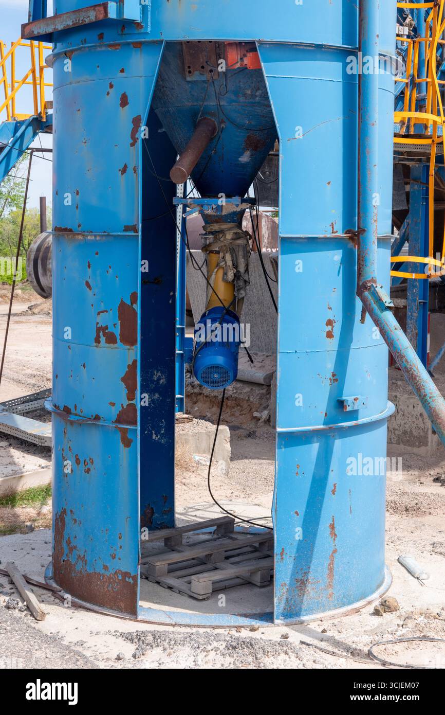 Grande silo blu industriale con motore elettrico sottostante, ruggine visibile e rimozione della vernice, ambiente di costruzione all'aperto Foto Stock