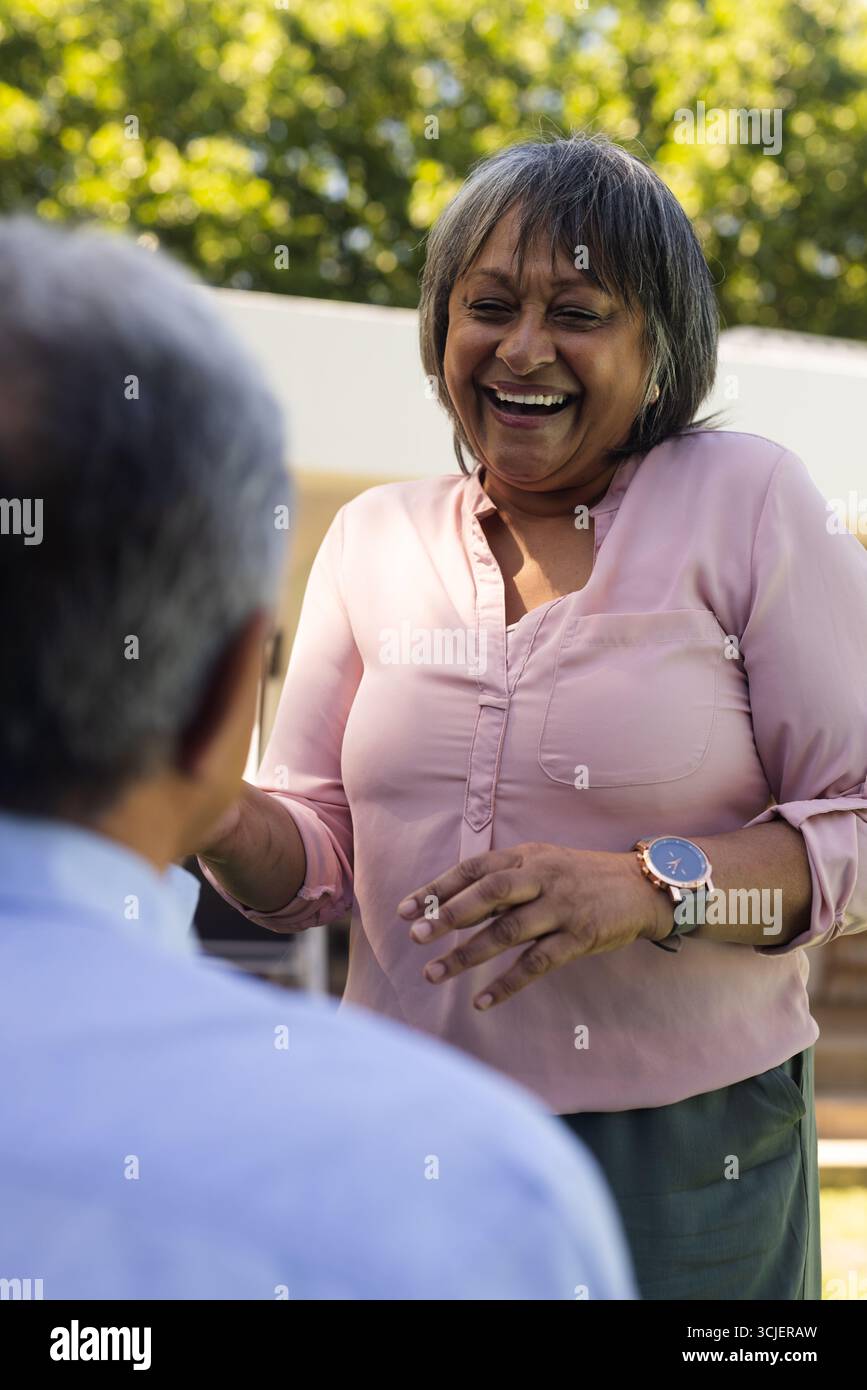 Donna sorridente che si diverte a conversare all'aperto con un amico in un parco soleggiato Foto Stock
