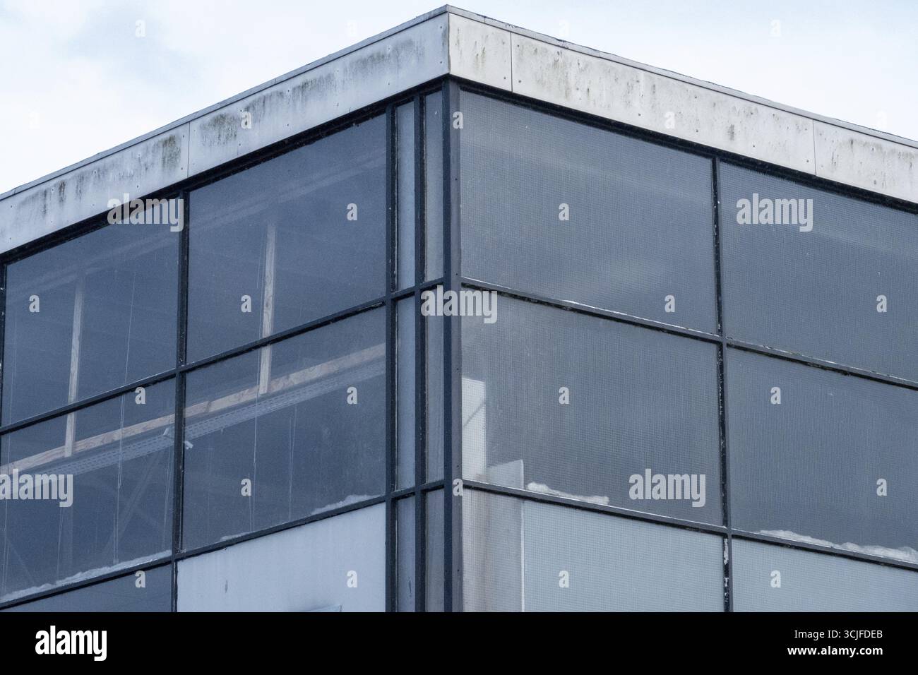 Facciata in vetro e cemento di un edificio modernista che mostra intemperie, sporcizia e finestre rotte, lasciando intendere l'abbandono e il degrado urbano Foto Stock
