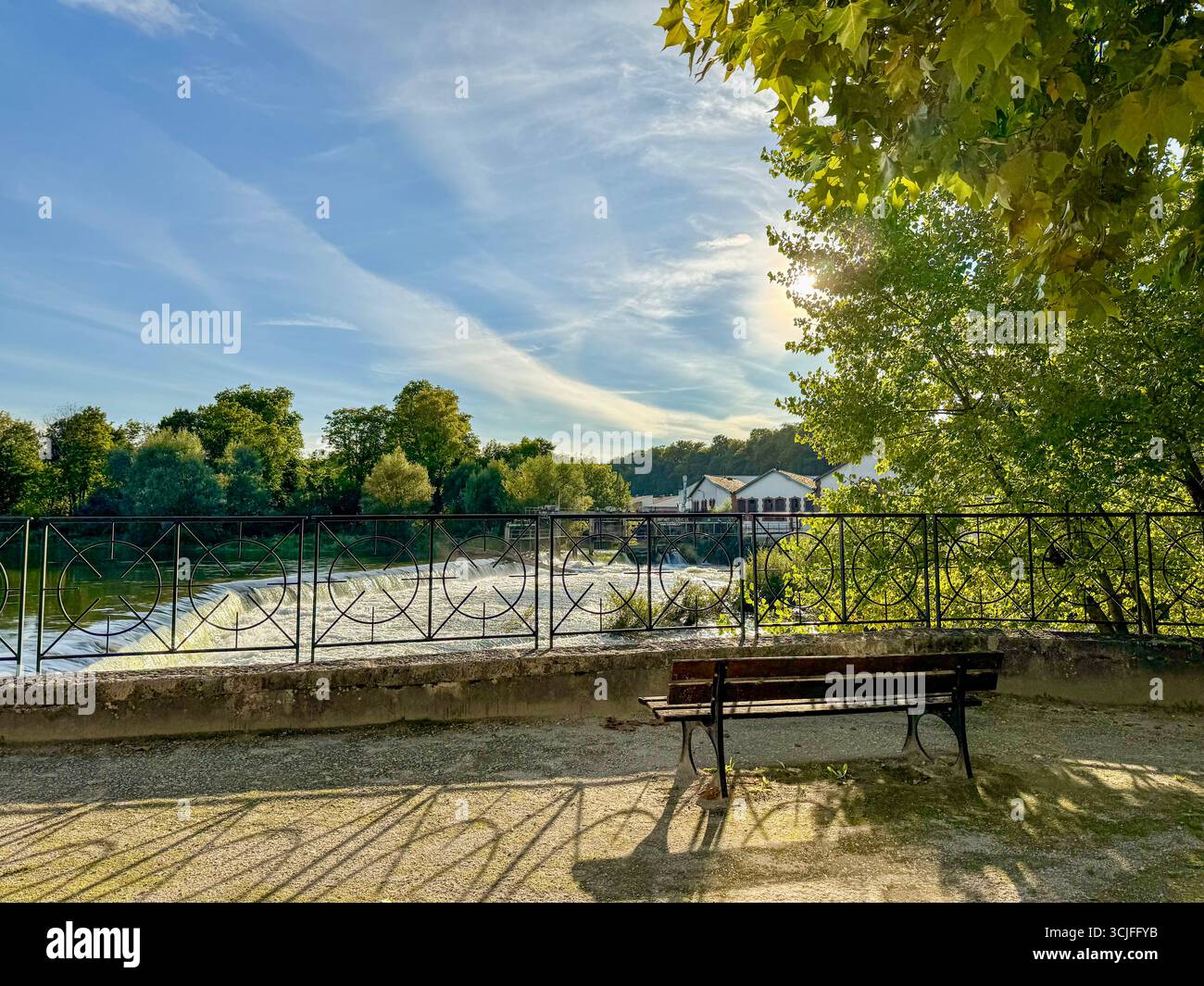 Panca in legno che si affaccia sullo sbarramento des Forges, con una vecchia fabbrica metallurgica lungo il fiume Doubs sotto la luce soffusa del sole. Foto Stock