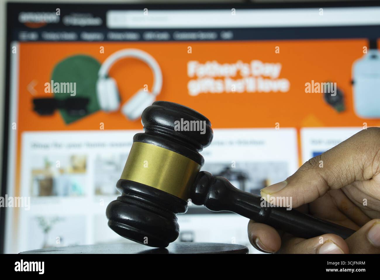 Dhaka, Bangladesh - 20 giugno 2025: Una mano tiene un martelletto davanti allo schermo di un computer che visualizza il sito web di Amazon Foto Stock