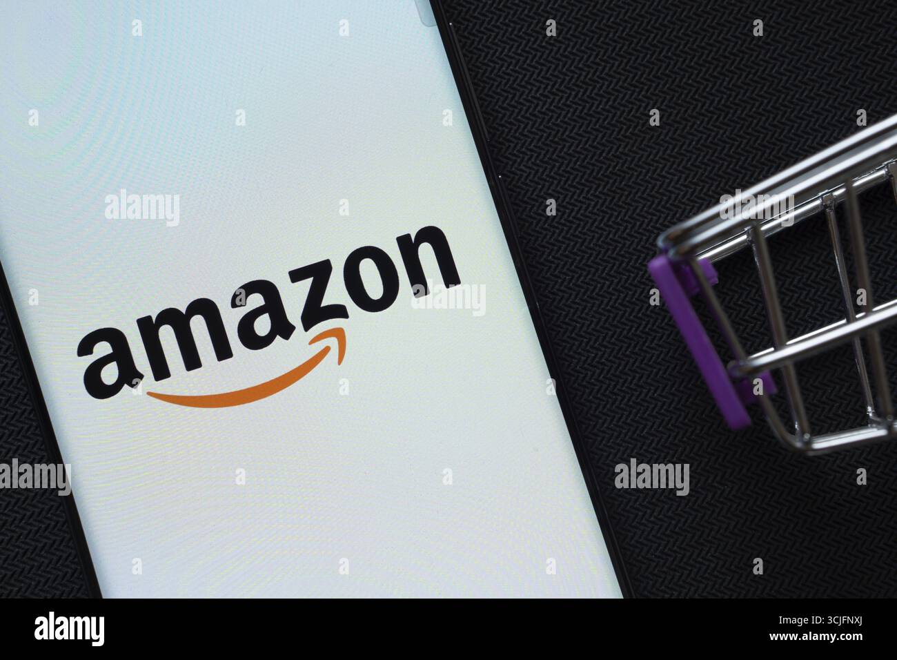 Dhaka, Bangladesh - 3 luglio 2025: Uno smartphone con il logo Amazon accanto a un carrello in miniatura sullo sfondo Foto Stock