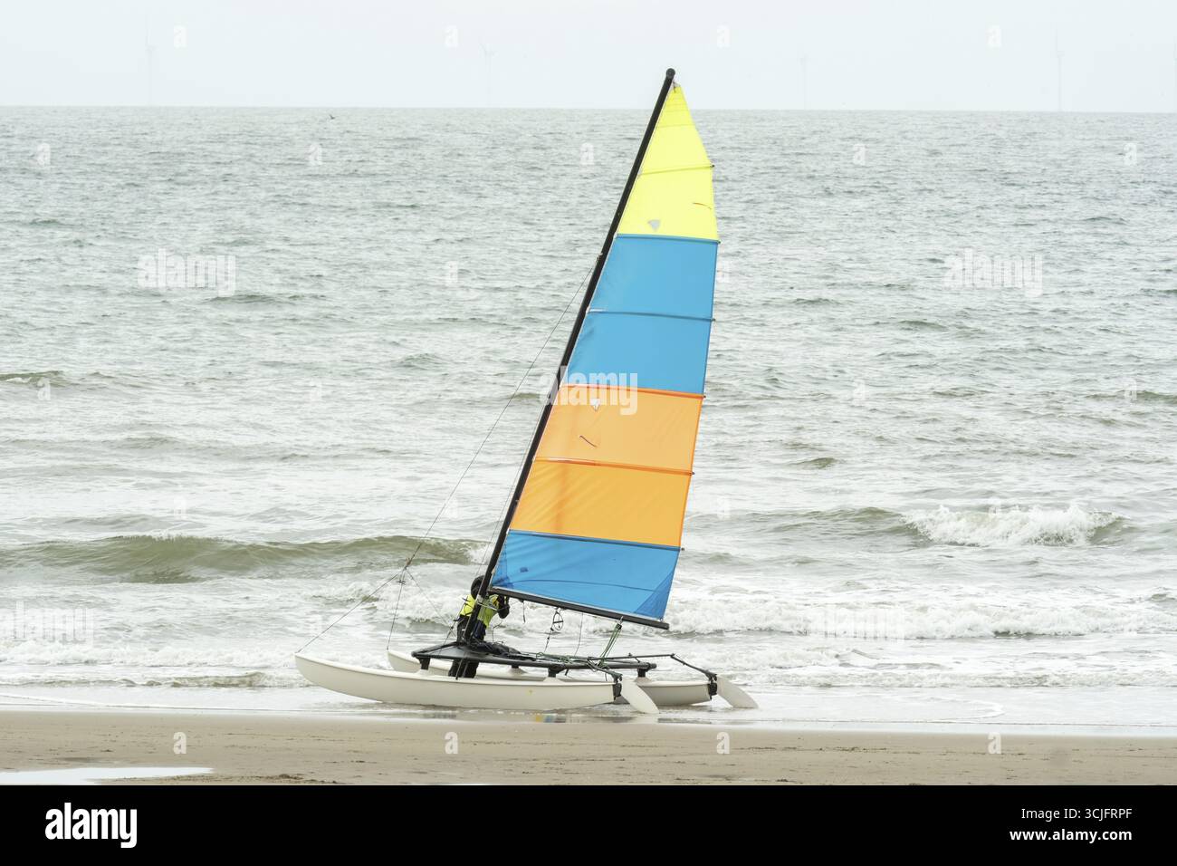 Piccolo catamarano con vela colorata che riposa su una spiaggia sabbiosa, pronto per avventure di sport acquatici Foto Stock