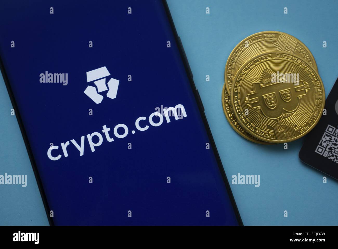 Dhaka, Bangladesh- 26 agosto 2025: Logo Crypto.com sullo schermo dello smartphone vicino alla moneta Bitcoin e codice QR su sfondo blu Foto Stock