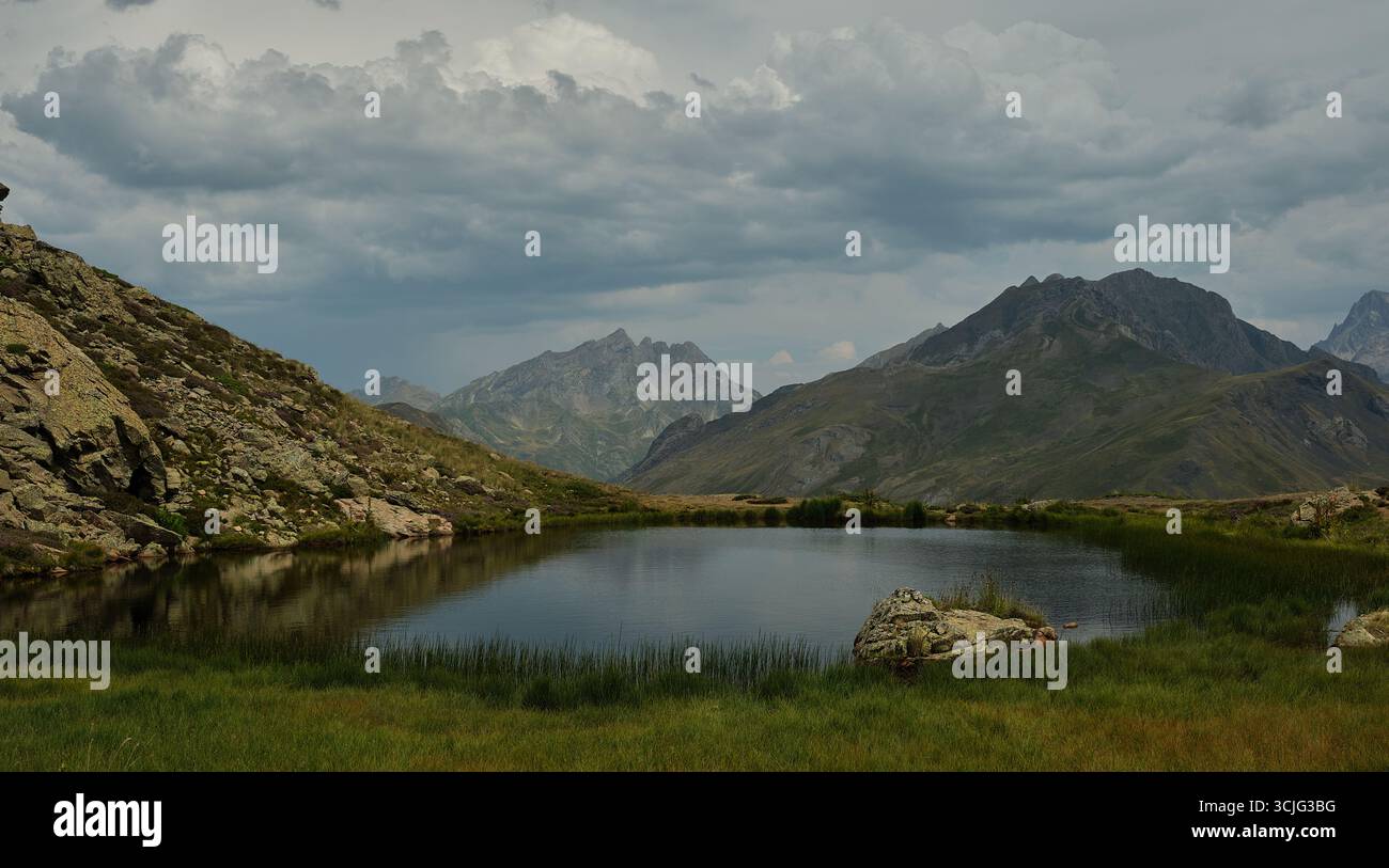 Fotografia di un piccolo lago in cima alla montagna, immagine della natura con nuvole nel cielo e un paesaggio alpino, una roccia in primo piano e una bellezza Foto Stock