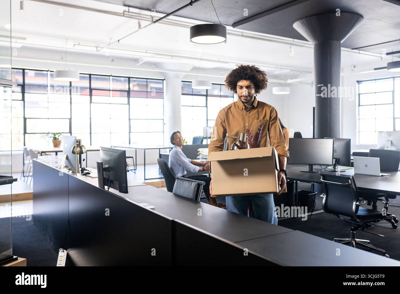 Uomo che trasporta una cassetta in un ufficio moderno, che si prepara per una nuova transizione di lavoro Foto Stock