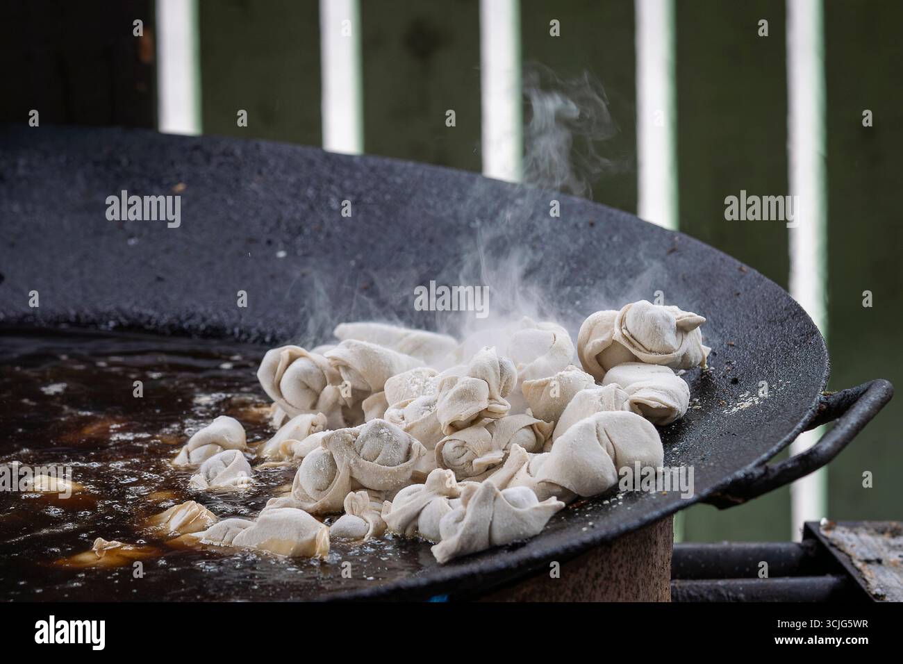 Pelmeni (gnocchi) friggere su una padella alla griglia durante il festival del cibo urbano. Lo chef prepara deliziosi pelmeni su una grigliata calda. Foto Stock