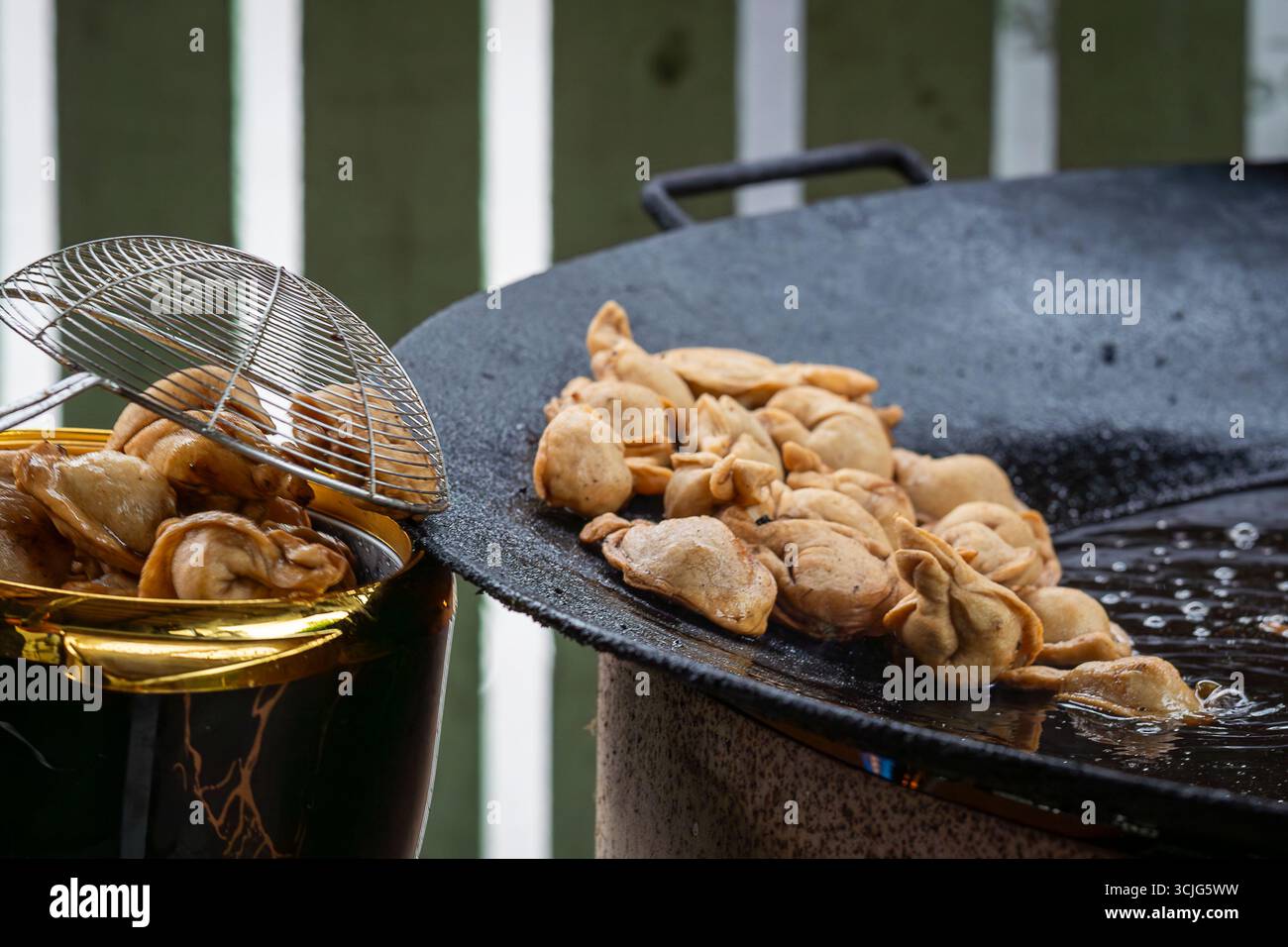 Pelmeni (gnocchi) friggere su una padella alla griglia durante il festival del cibo urbano. Lo chef prepara deliziosi pelmeni su una grigliata calda. Foto Stock