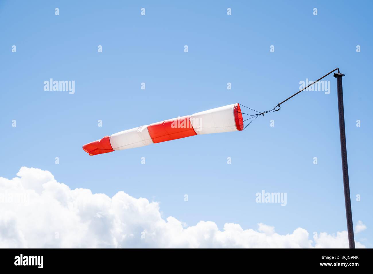 Calza a vento a righe bianco-rosso contro un cielo azzurro limpido con soffici nuvole bianche in estate come indicazione per il vento Foto Stock