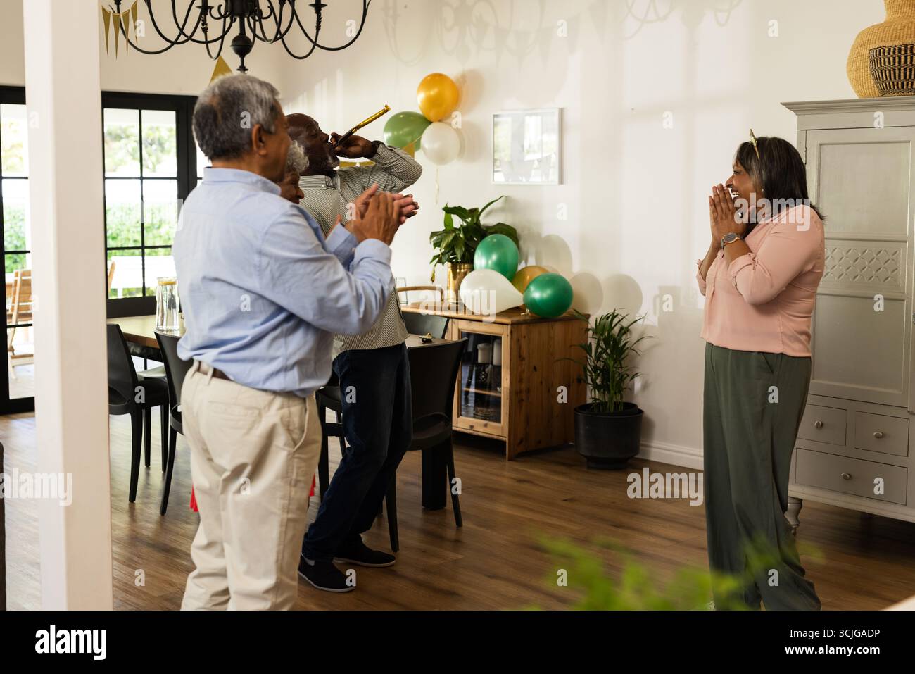 Festeggia una festa a sorpresa a casa, amici anziani con palloncini, espressioni gioiose Foto Stock