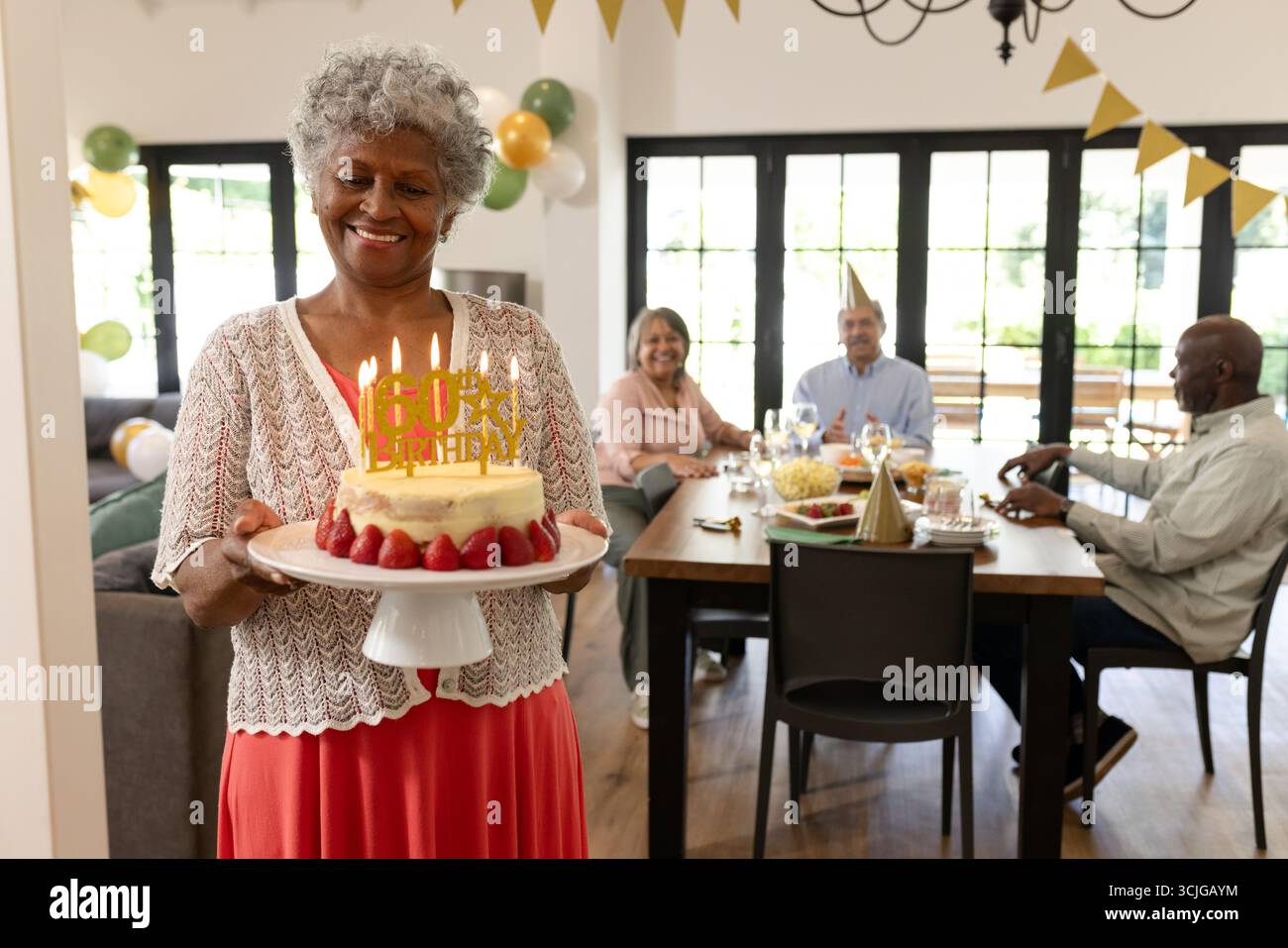 Donna anziana che porta la torta di compleanno con le candele, sorridente alla riunione di famiglia Foto Stock