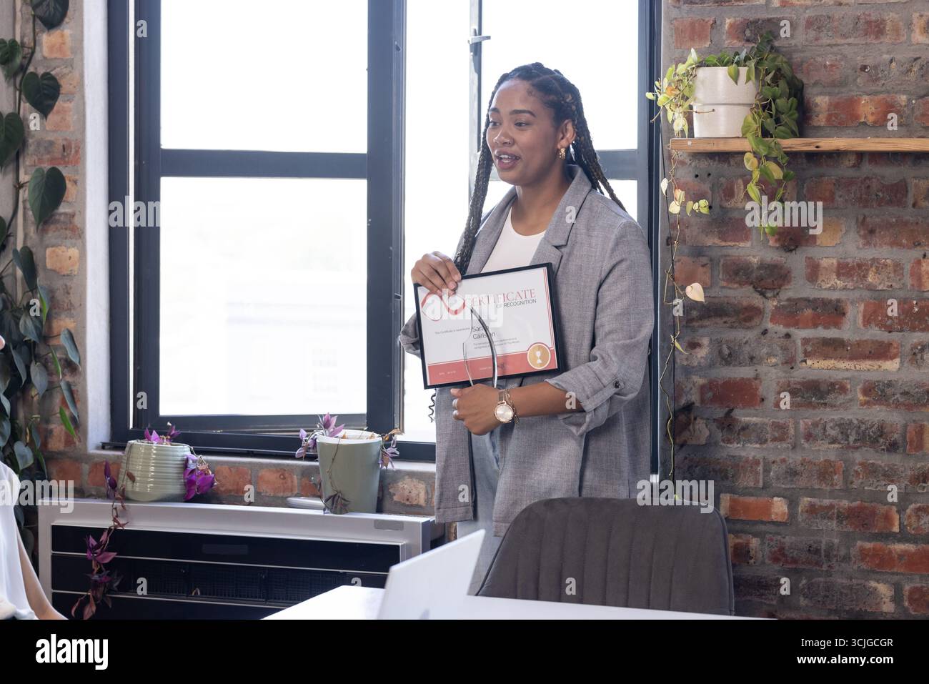 In possesso del certificato, donna afroamericana sorridente orgogliosamente durante l'evento di celebrazione dell'ufficio Foto Stock