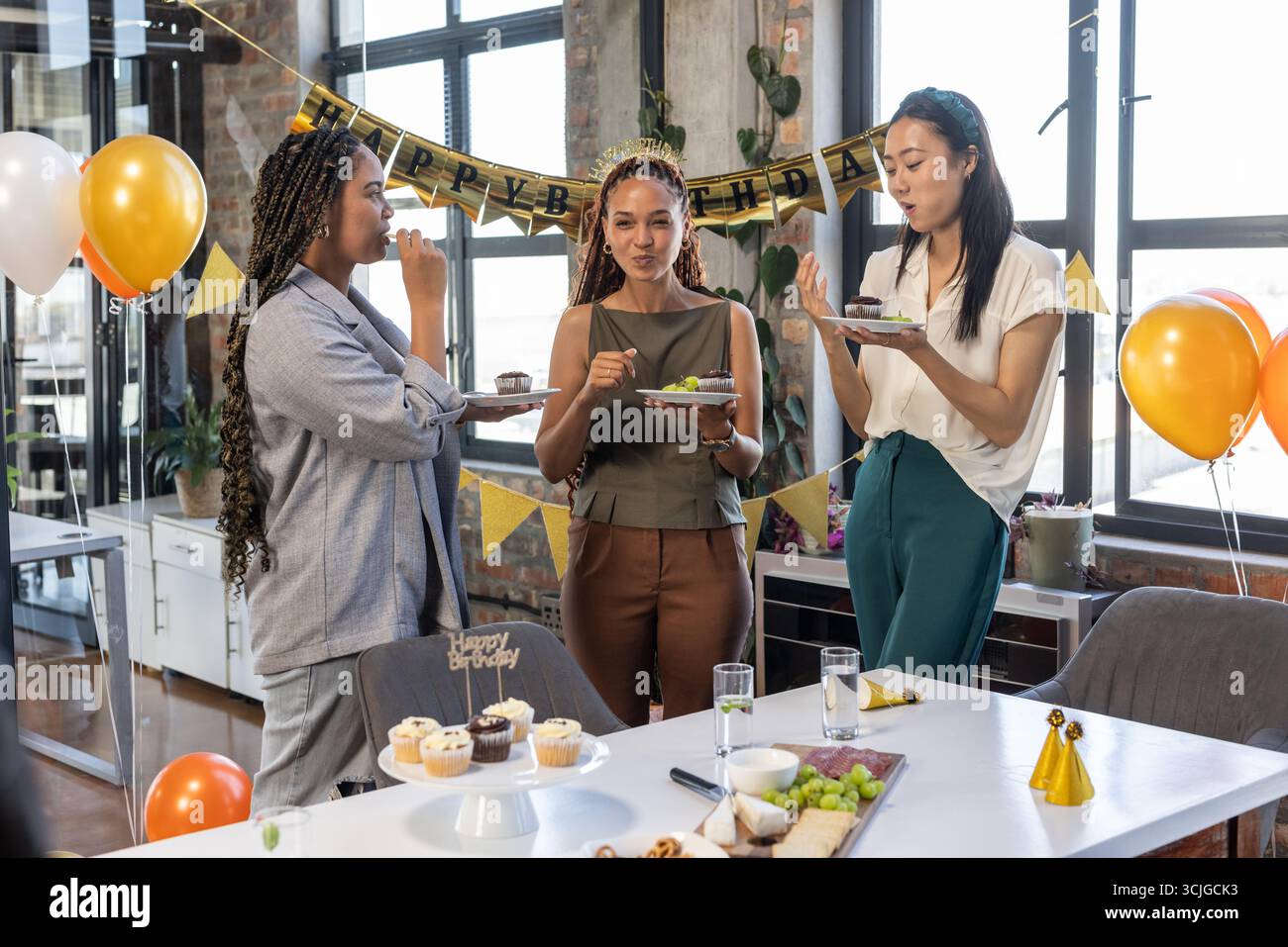 I colleghi si godono la festa di compleanno con torte e palloncini in un ufficio moderno Foto Stock