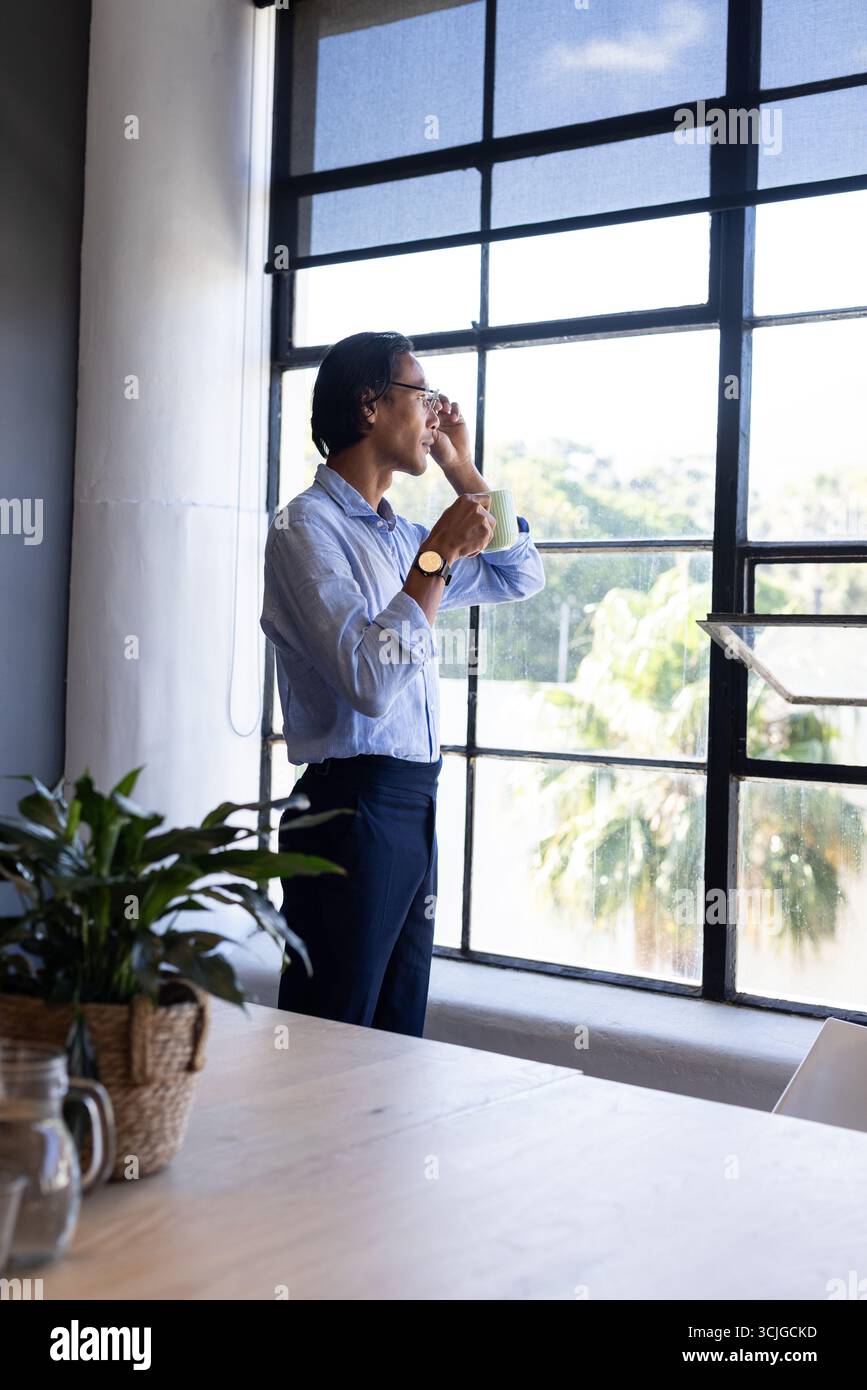 Uomo d'affari in piedi davanti alla finestra, con caffè, con smartphone in ufficio Foto Stock