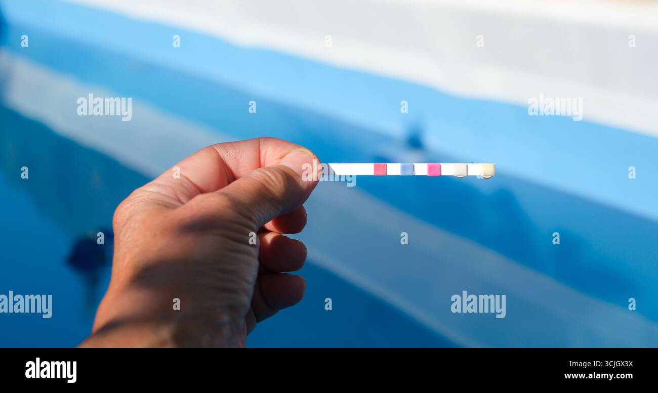 Striscia di test in piscina nella mano umana su sfondo Blue Pool. PH. Acqua di piscina Bilancio idrico. Concetto di chimica del pool. Foto Stock