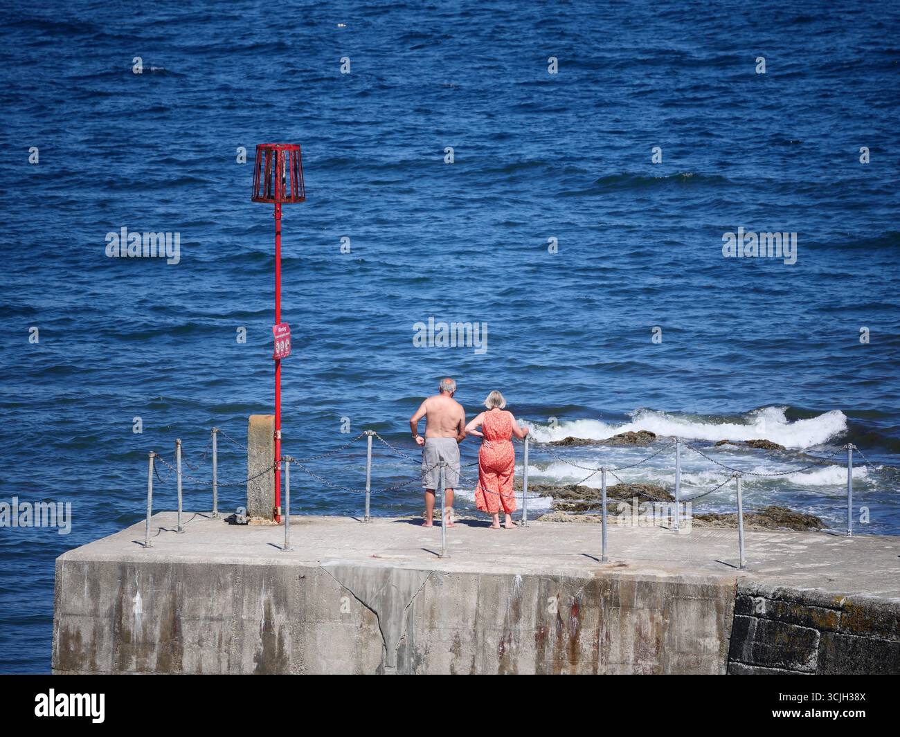 Una coppia più anziana si affacciava sul mare da un muro del porto in un caldo giorno d'estate. Cornovaglia, Regno Unito Foto Stock