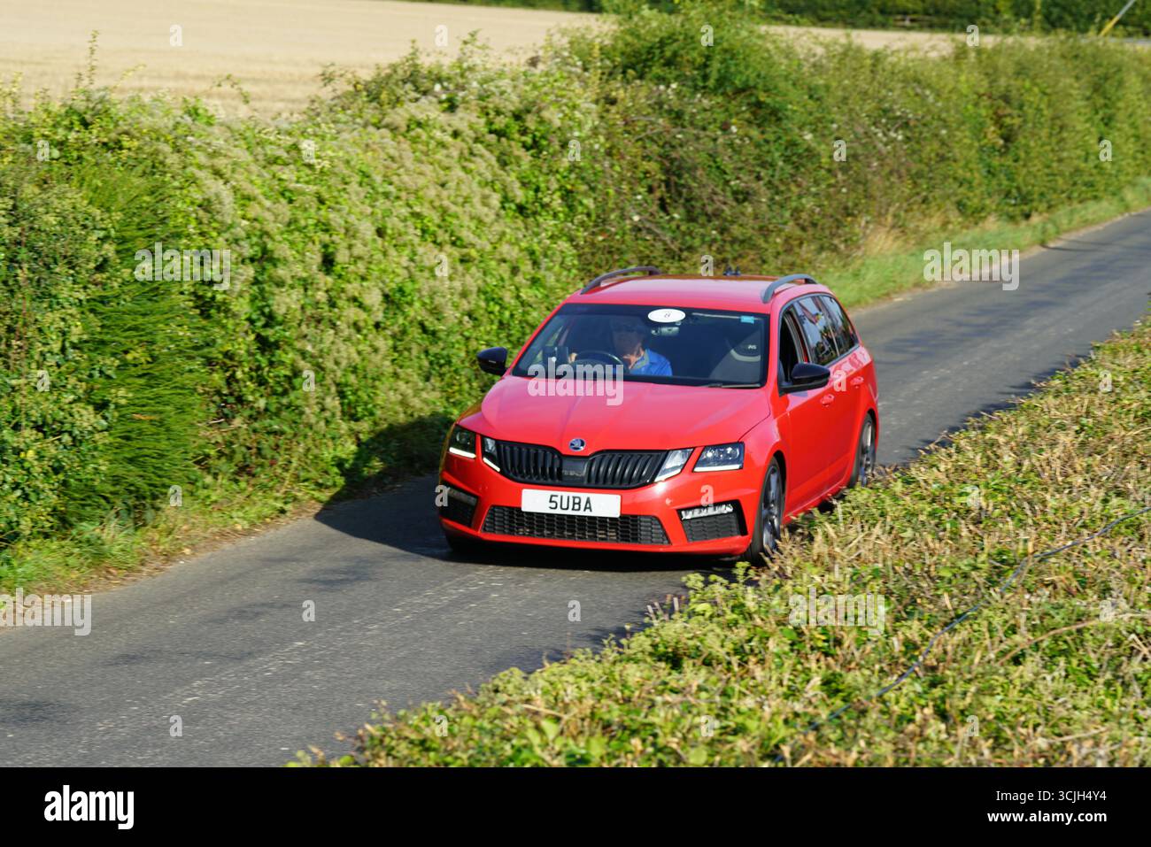 Auto rossa moderna che guida attraverso una strada panoramica di campagna durante il giorno. Shere Hill Climb, East Clandon, Guildford Foto Stock