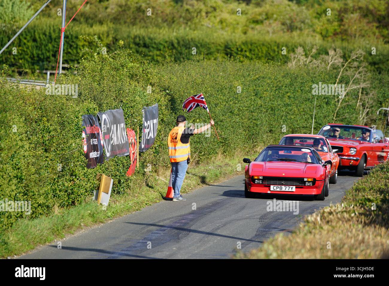 Corse automobilistiche classiche su una strada rurale con bandiera ufficiale dell'evento. Shere Hill Climb, East Clandon, Guildford Foto Stock