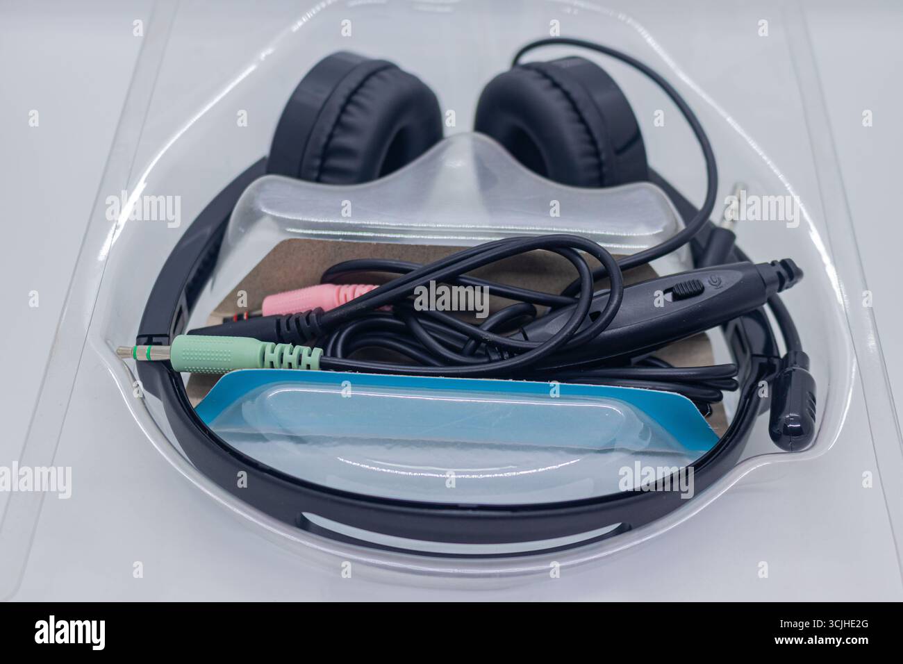 Cuffie nere avvolgenti con microfono integrato in confezione blister su sfondo bianco isolato. Foto Stock