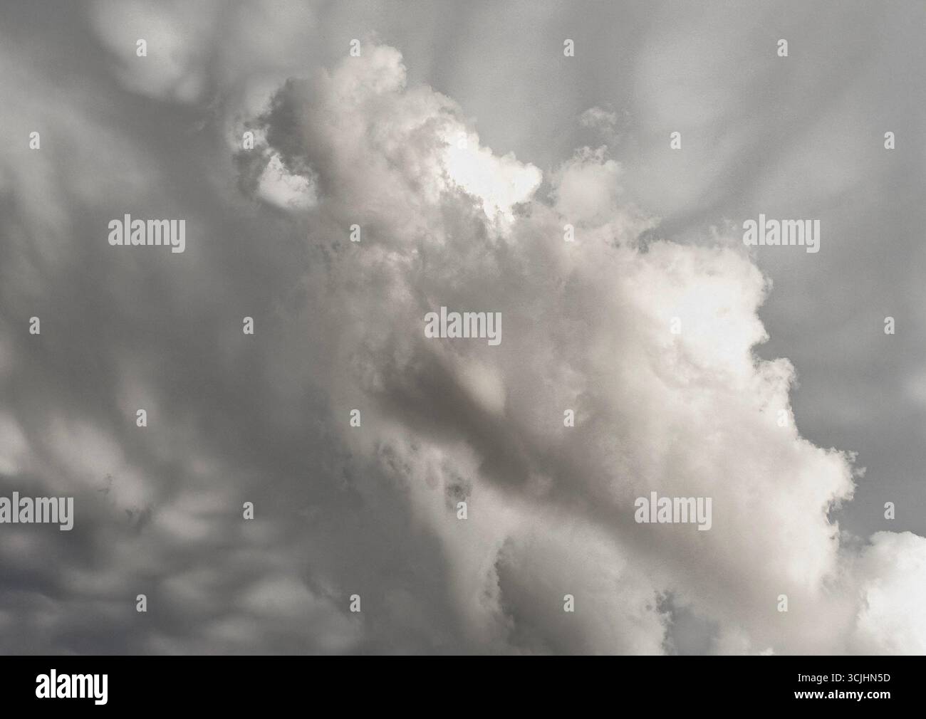 Spettacolare paesaggio nuvoloso in scala di grigi con torreggianti formazioni di cumulus che proiettano ombre morbide nel cielo. L'interazione tra luce e buio conferisce un aspetto lunatico, alm Foto Stock