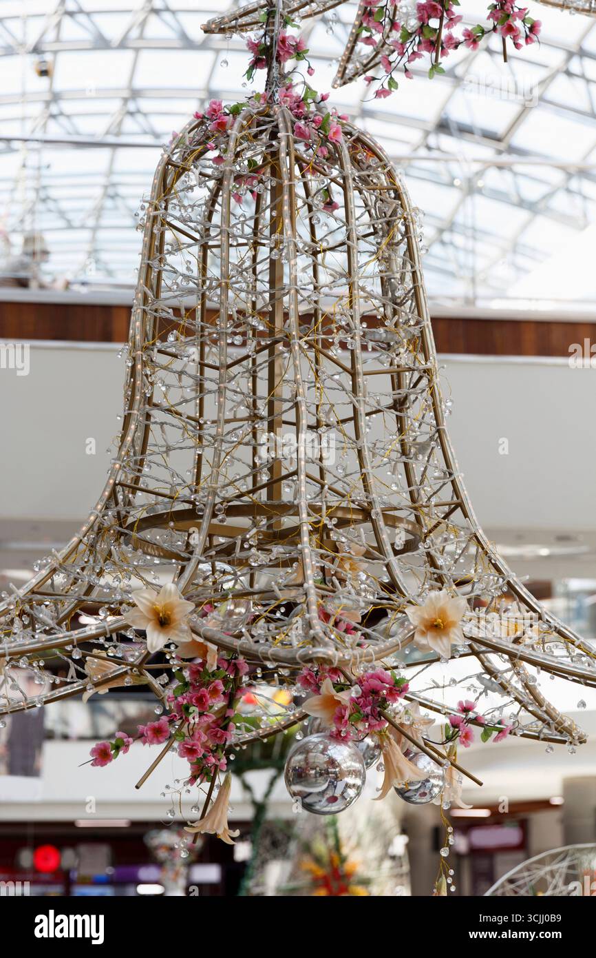 Un lampadario decorativo a forma di campana realizzato in materiali tessuti, adornato da fiori e cristalli appesi. Viene visualizzato in uno spazio interno luminoso con Foto Stock