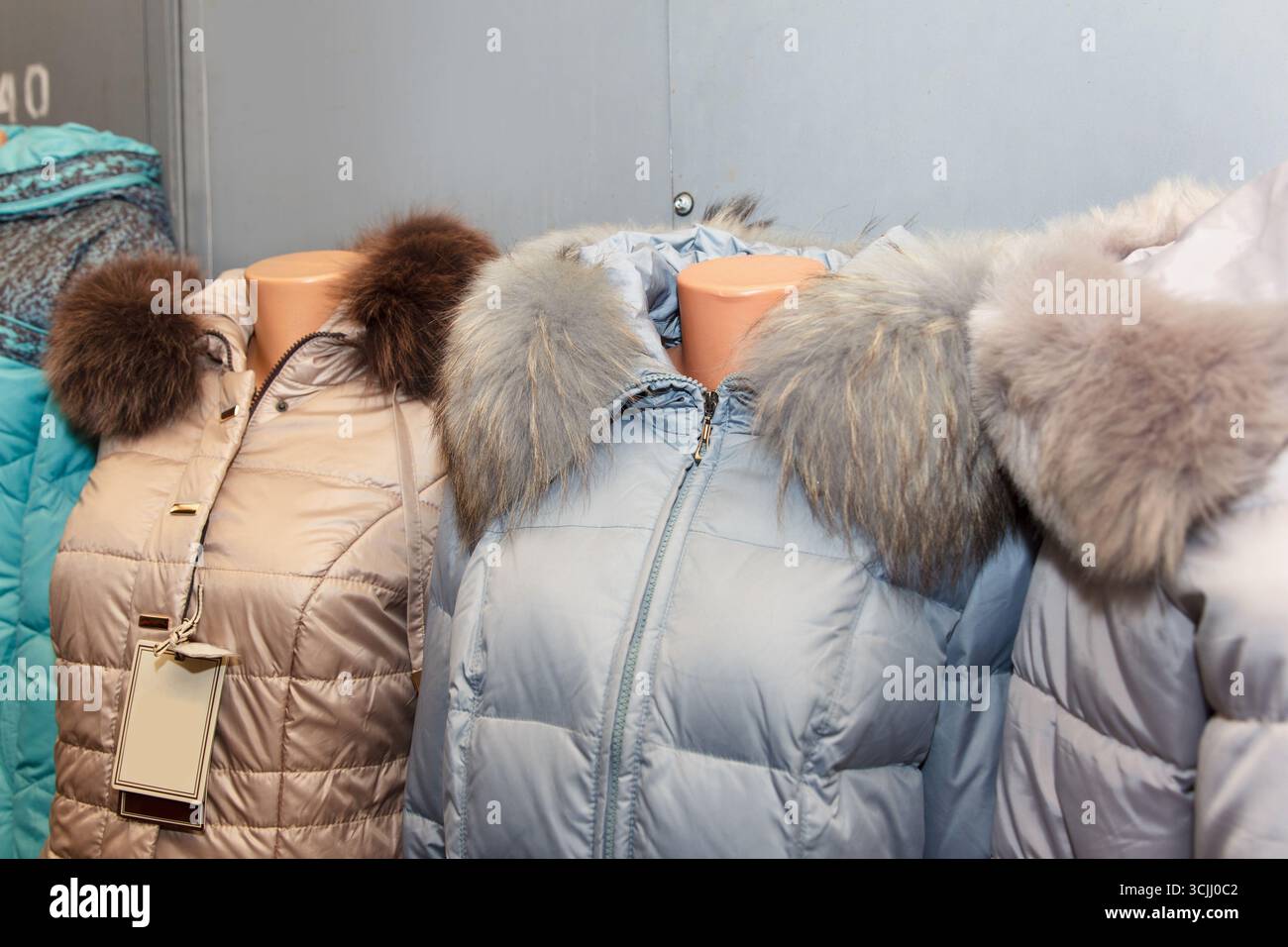 Fila di calde giacche invernali con colletti in pelliccia su manichini, in vari colori, su uno sfondo interno. Concetto di outerwear alla moda Foto Stock