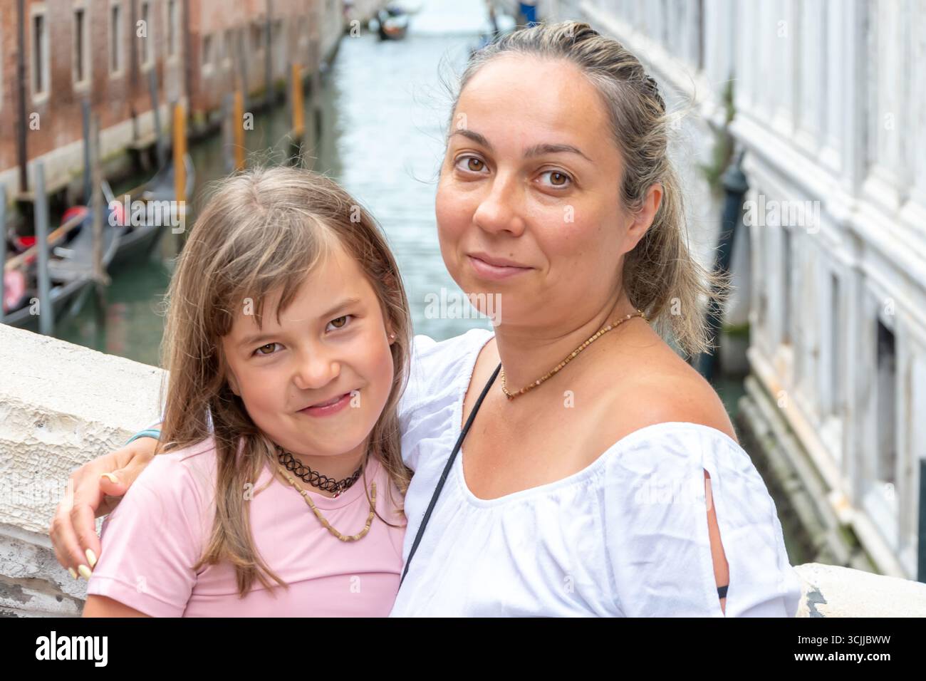 Ritratto di strada, madre che abbraccia sua figlia sullo sfondo di un canale e di edifici storici a Venezia Foto Stock