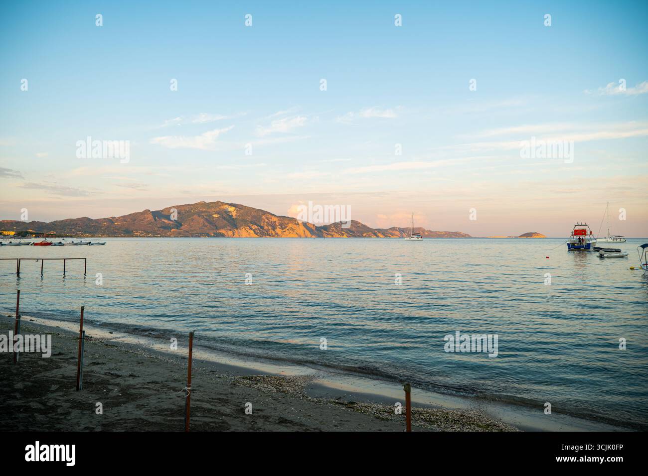 Vista panoramica della baia di Laganas, Zante, Grecia, con una barca a vela che galleggia sul mare e colline rocciose in una calda luce serale sotto il cielo limpido Foto Stock Vista panoramica della baia di Laganas, Zante, Grecia, con una barca a vela che galleggia sul mare e colline rocciose in una calda luce serale sotto il cielo limpido Foto Stock