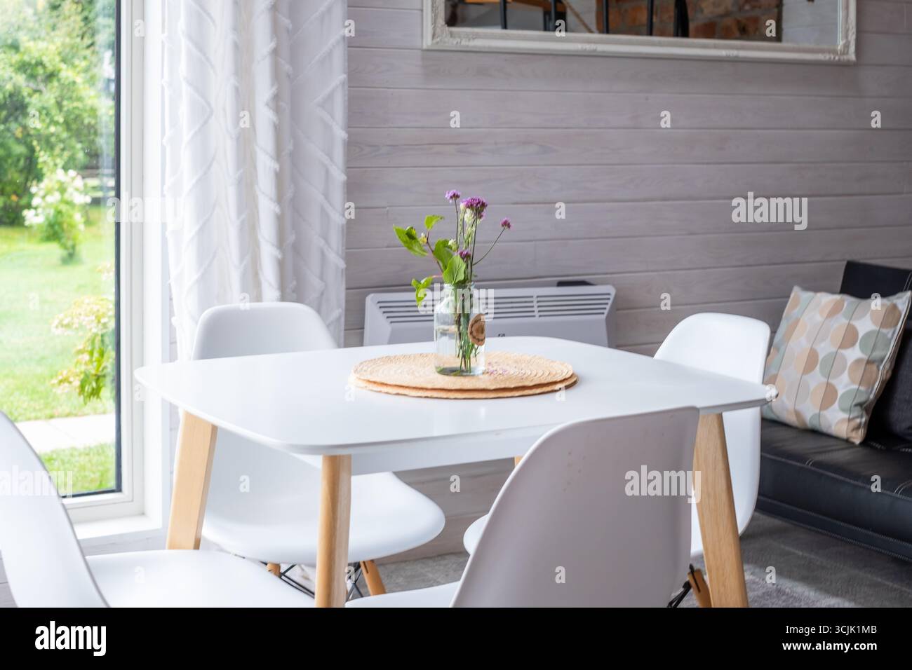 L'area da pranzo scandinava minimalista presenta un tavolo bianco, comode sedie e luce naturale, che esaltano l'atmosfera luminosa e ariosa con funzionalità Foto Stock